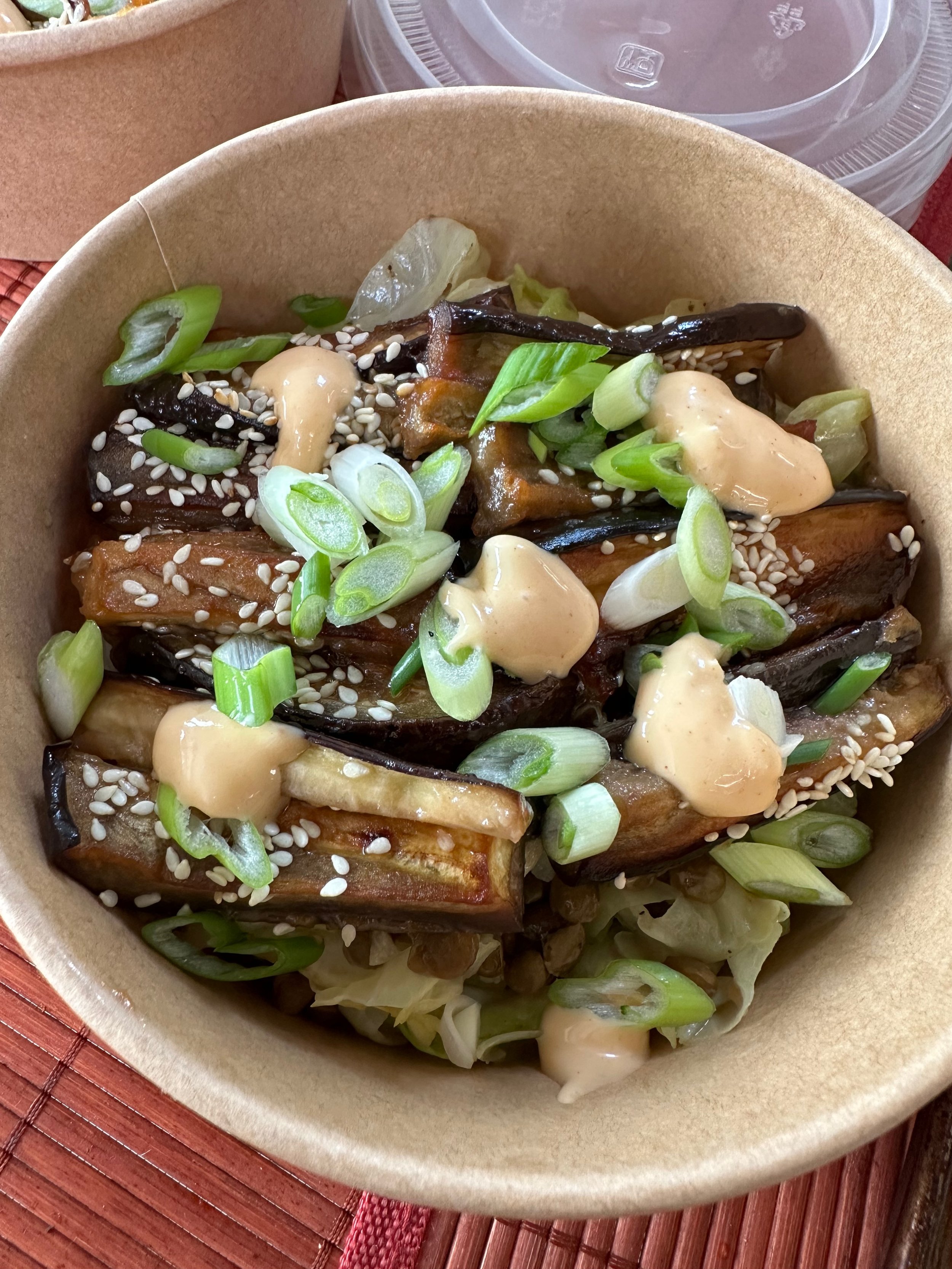 A bowl of roasted eggplant topped with green onions, sesame seeds, and a creamy sauce.