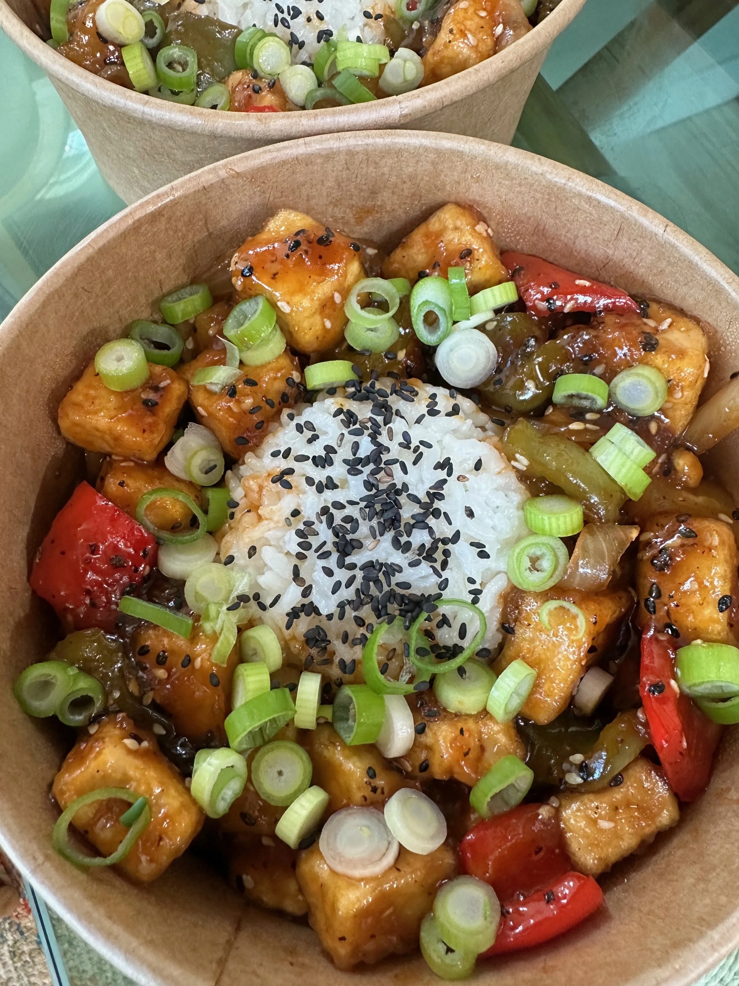 Close-up of a bowl of Chinese tofu with vegetables, topped with green onions and black sesame seeds.