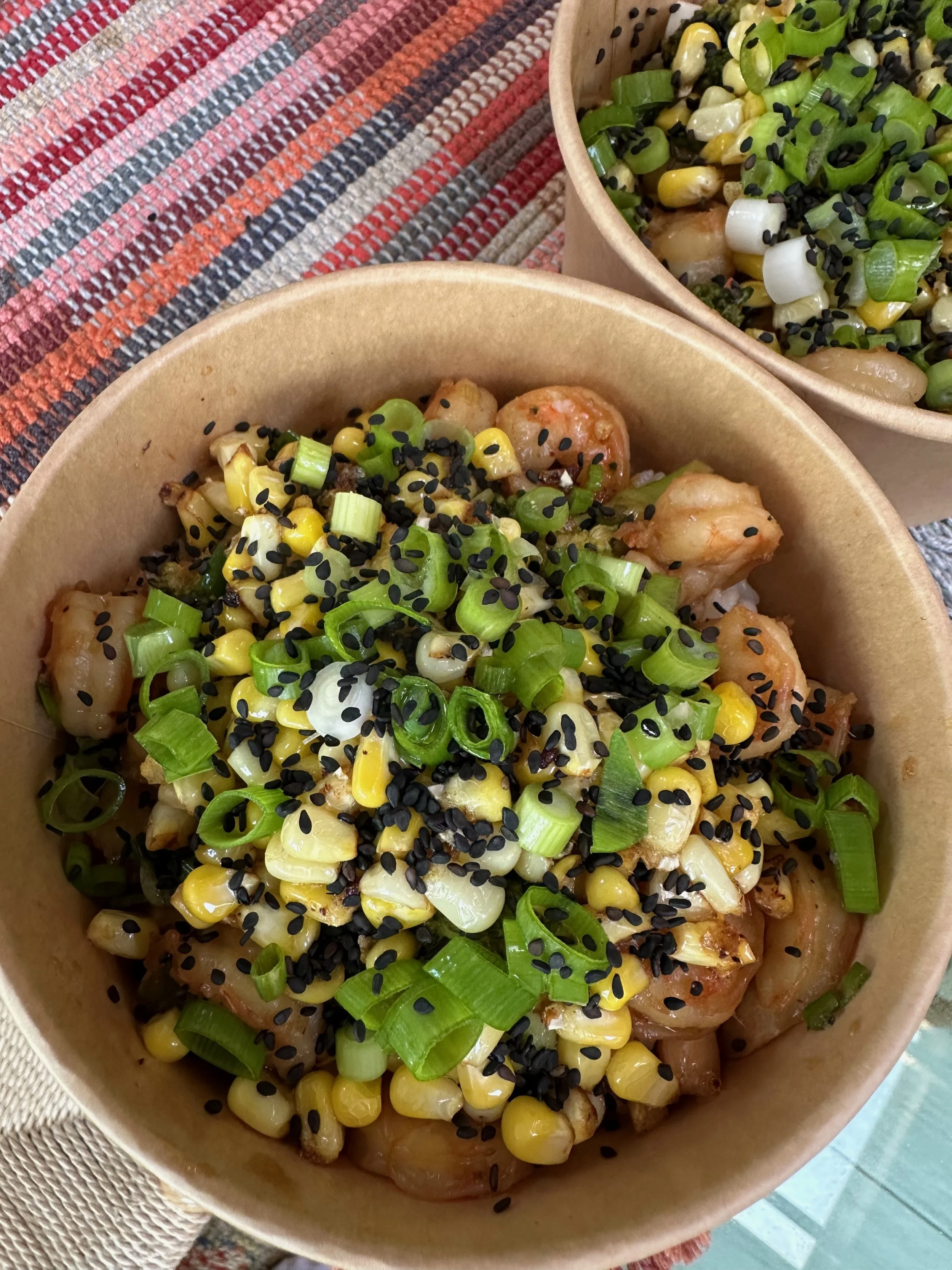 Bowls of poke with chopped green onions, black sesame seeds, corn, and chopped green onions on top.