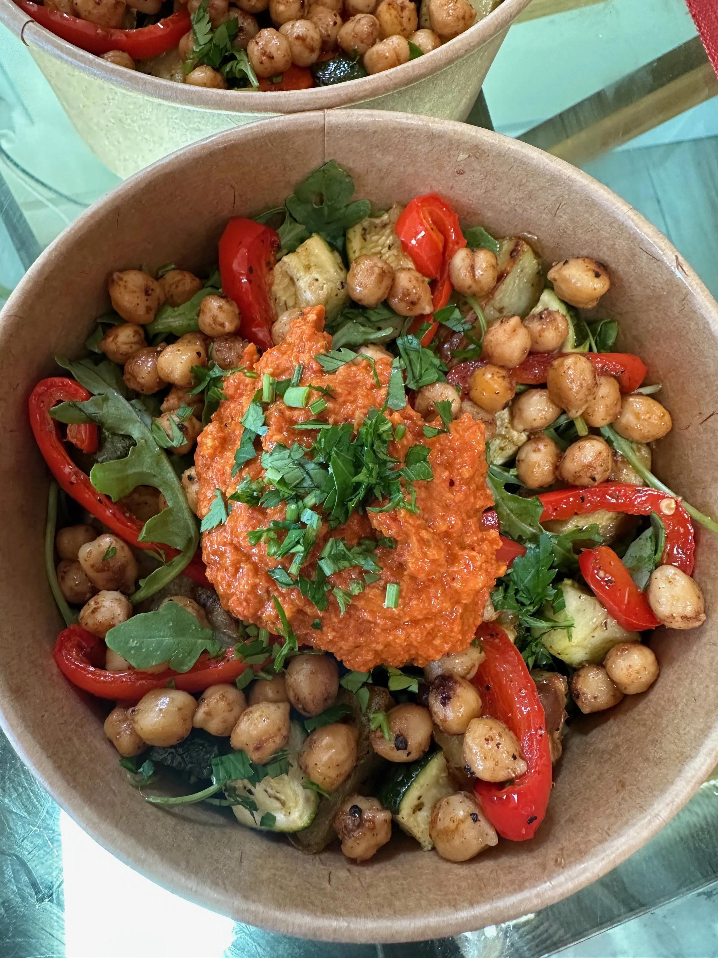 A bowl of chickpea salad with roasted red peppers, cucumber, and chopped herbs, topped with a dollop of red sauce and garnished with chopped green herbs.