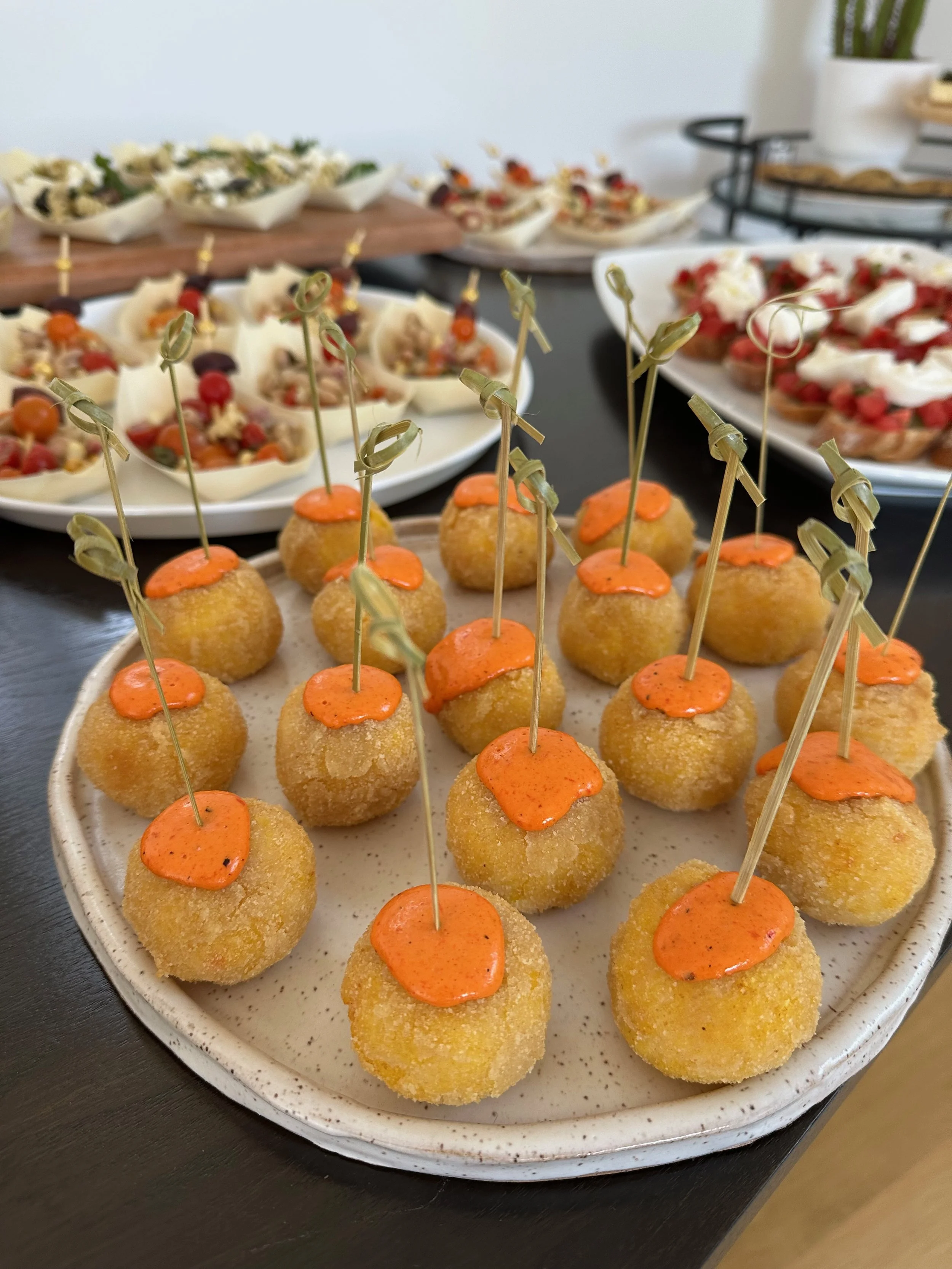 Plate of fried appetizers topped with orange sauce and skewers, with other appetizer dishes in the background.