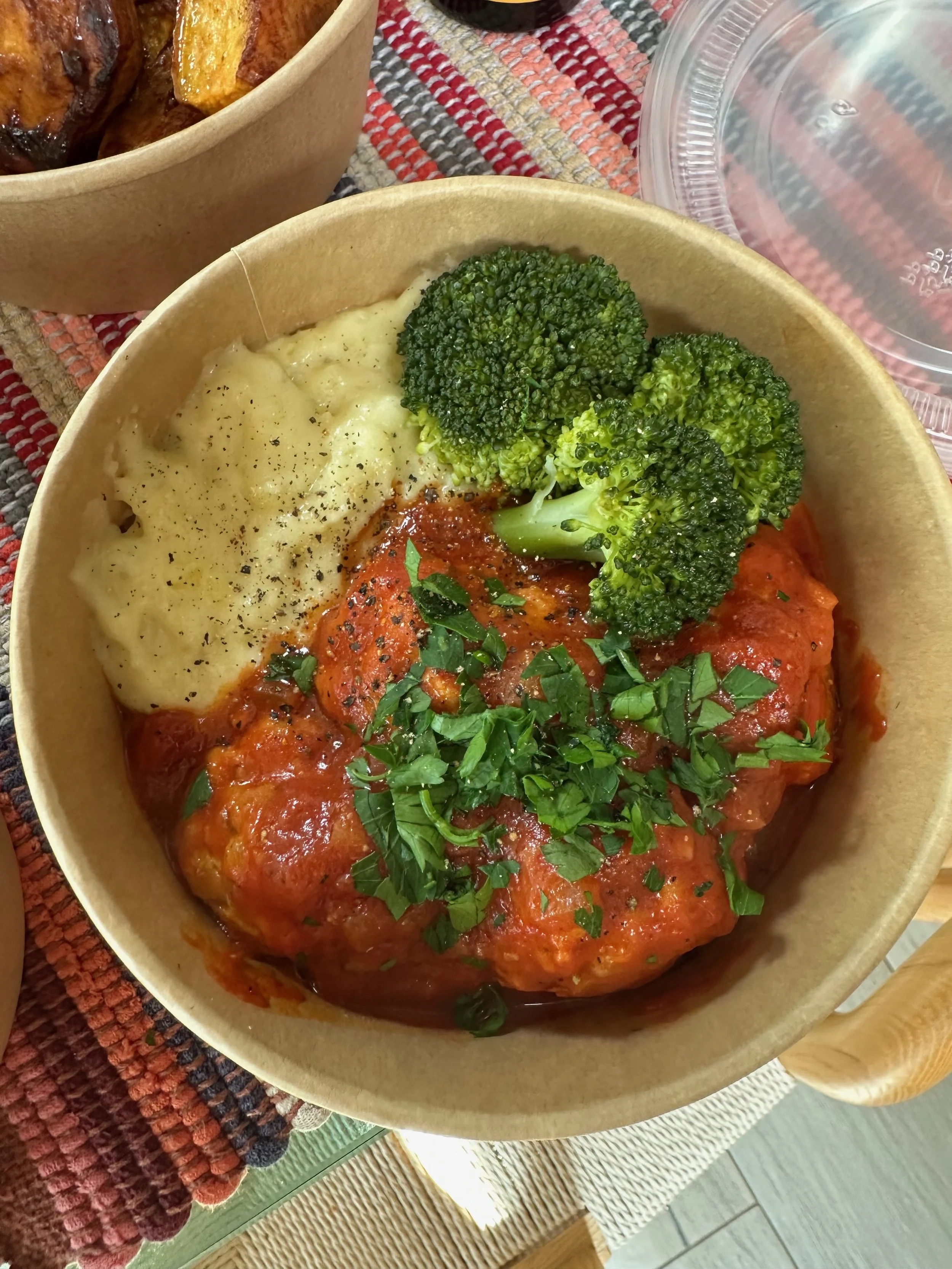 Bowl containing mashed potatoes, steamed broccoli, and a piece of meat covered in tomato sauce and chopped herbs.