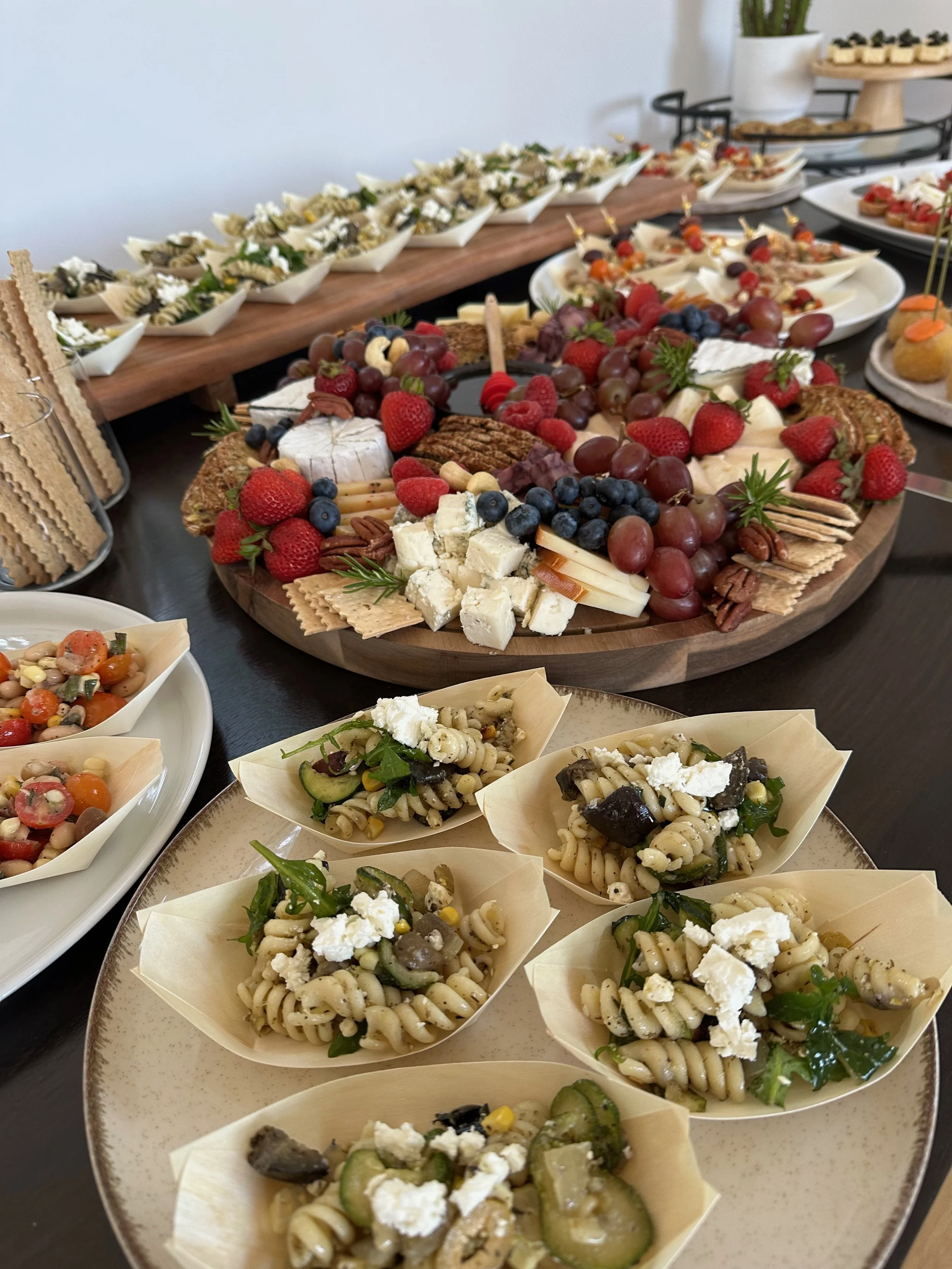 Assorted cheeses, fresh berries, and pasta salads on a table at a party or gathering.