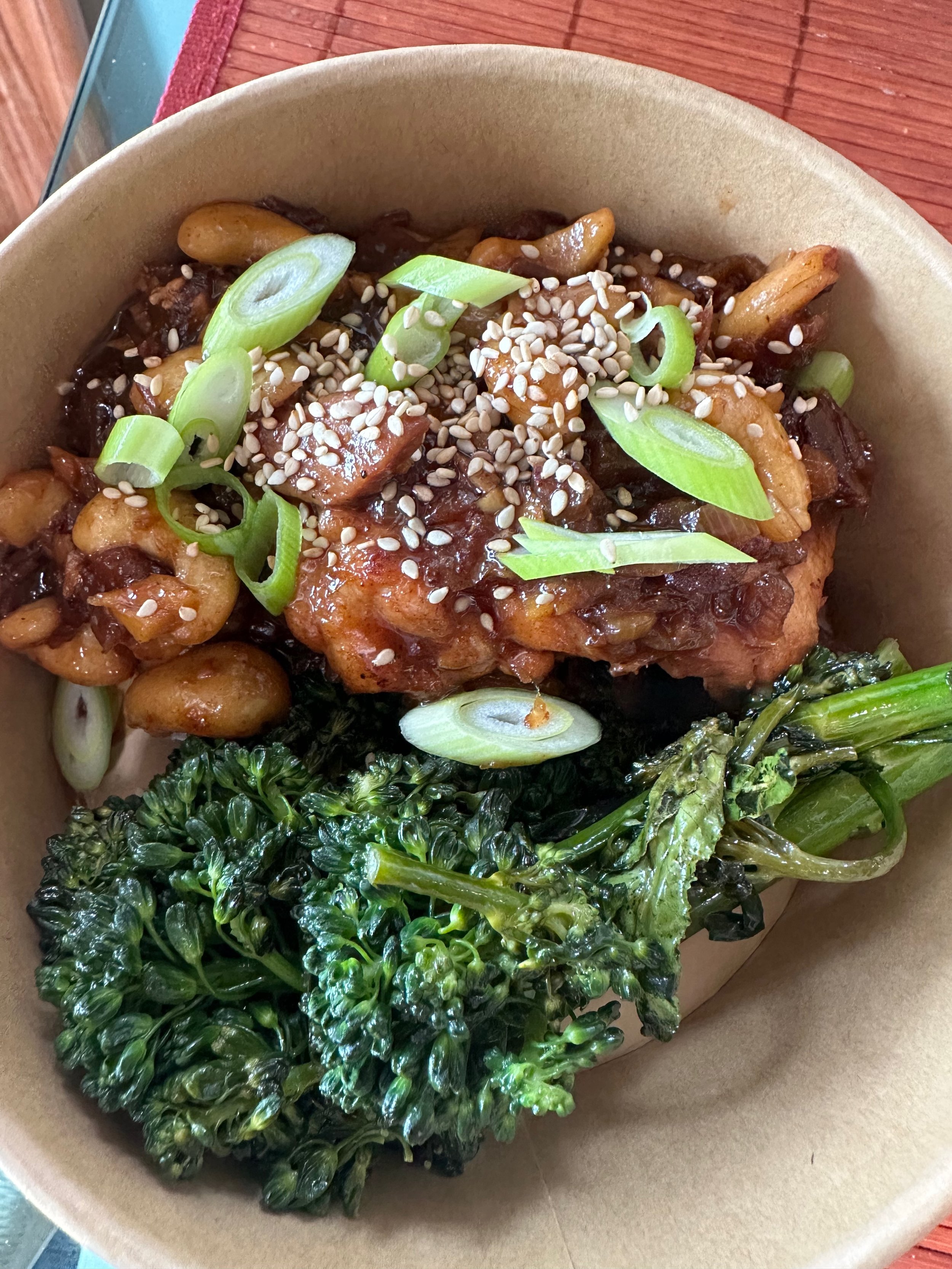 A bowl of Asian-inspired dish with chicken, vegetables, chopped green onions, sesame seeds, and sauce.