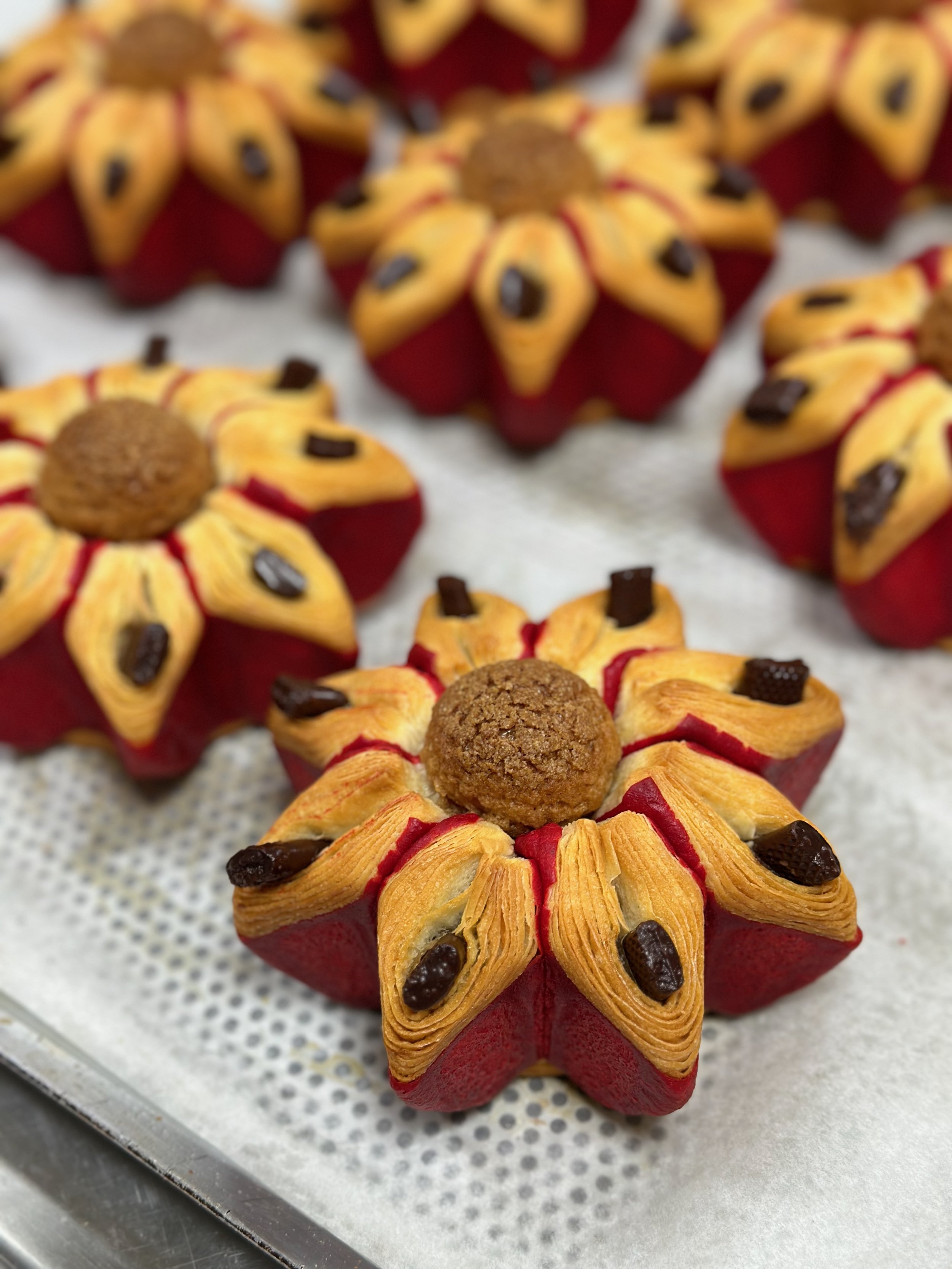 Decorative pumpkin-shaped pastries with piped frosting resembling petals, topped with a small cookie and chocolate chips, arranged on a parchment-lined tray.