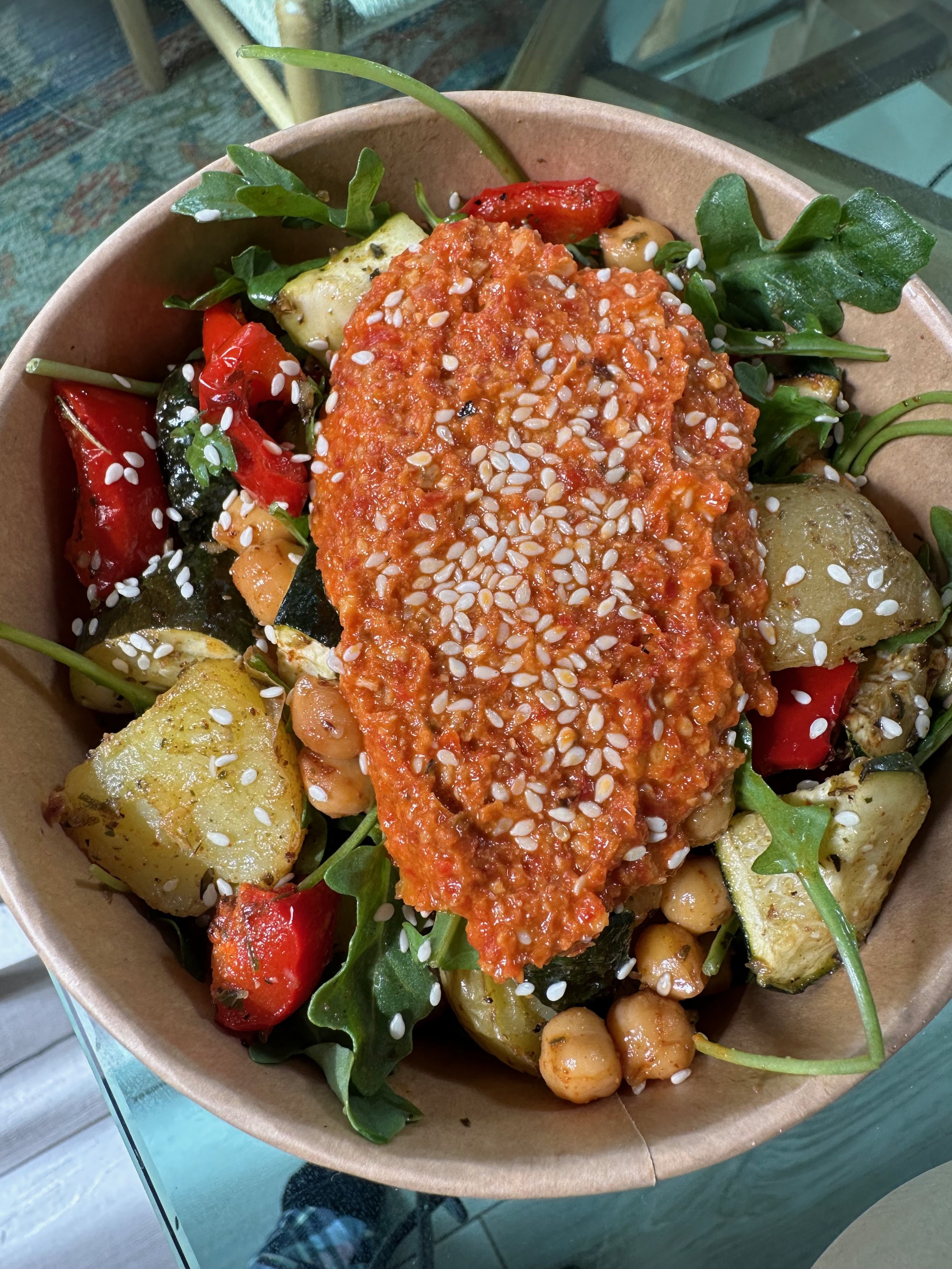 Salad with roasted potatoes, cherry tomatoes, chickpeas, arugula, and a red sauce with sesame seeds on top