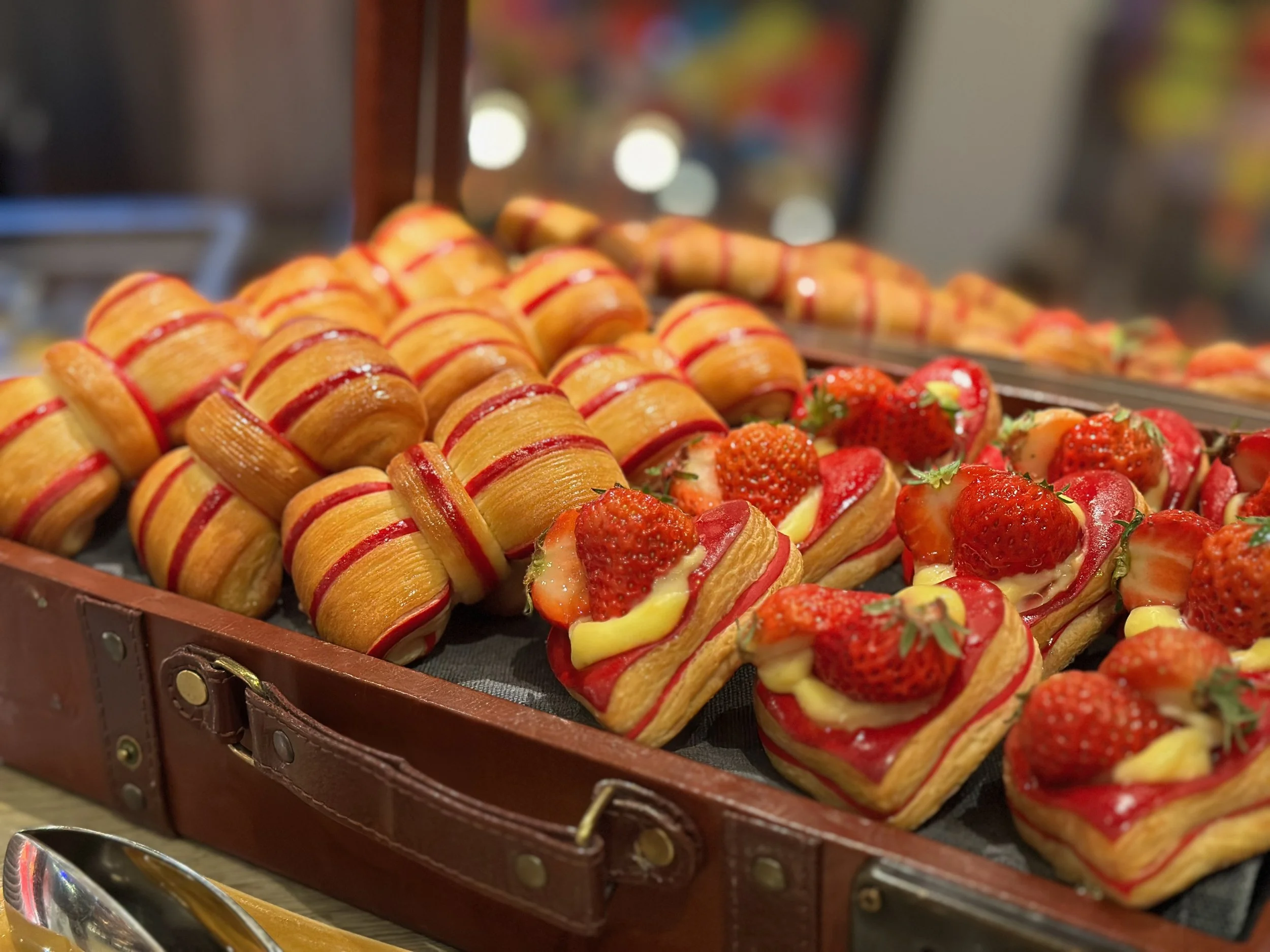 Assorted pastries including strawberry cream tarts and layered puff pastry treats with strawberries and yellow cream inside a display tray.
