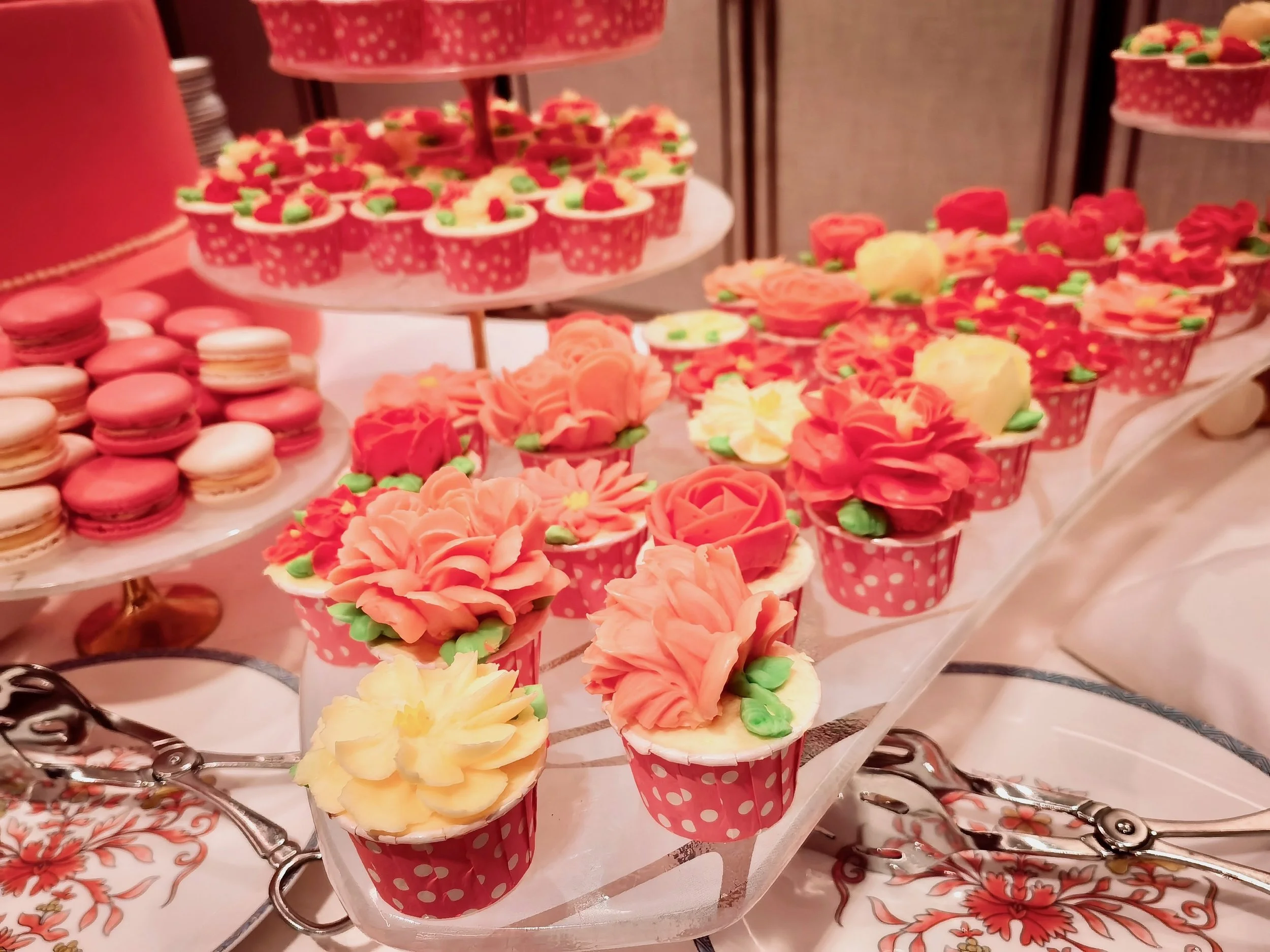 Assorted decorated cupcakes and macarons on a dessert table, including floral and polka dot patterns.