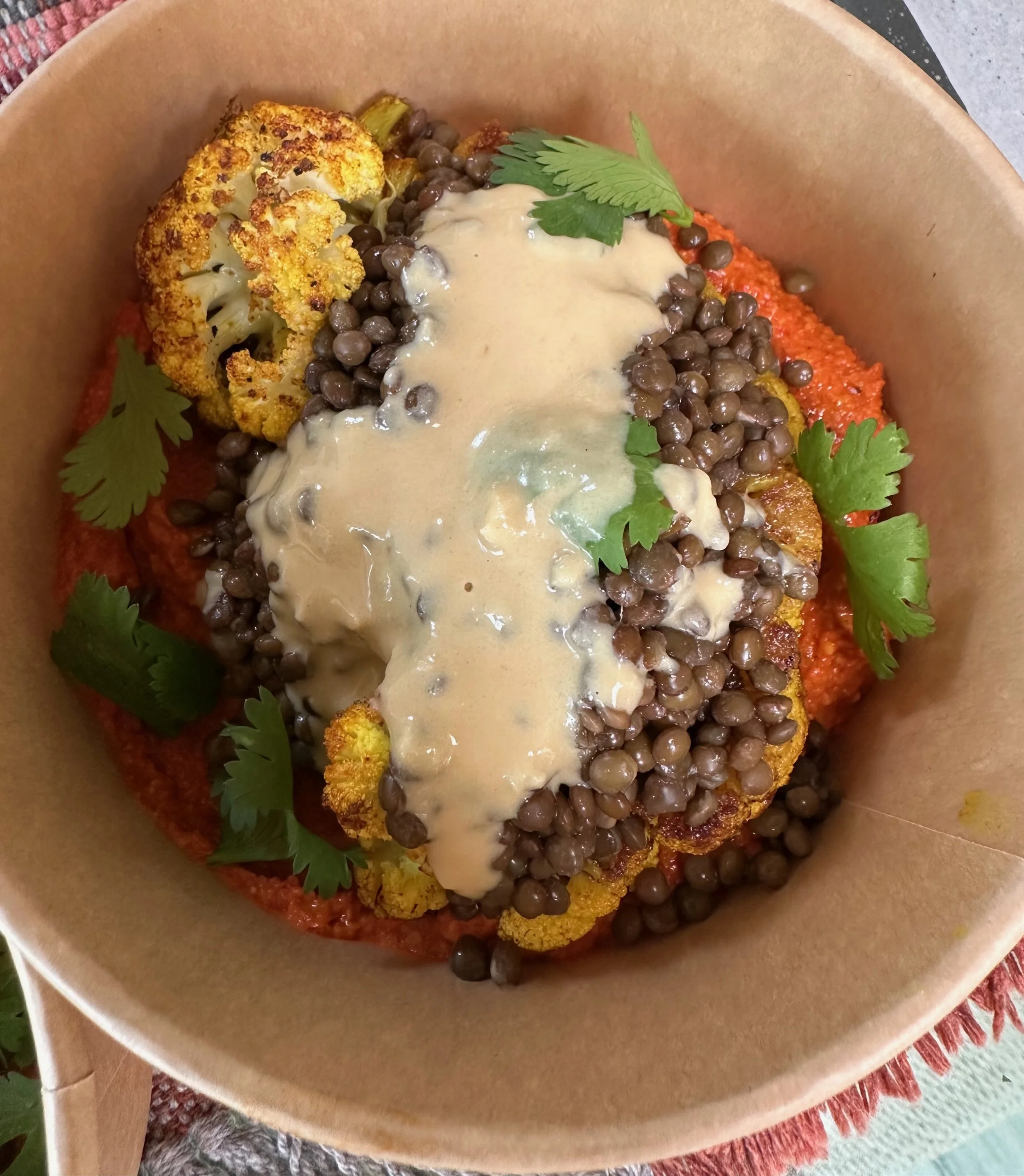 A bowl of roasted cauliflower, black lentils, red sauce, fresh cilantro, topped with creamy tahini dressing.