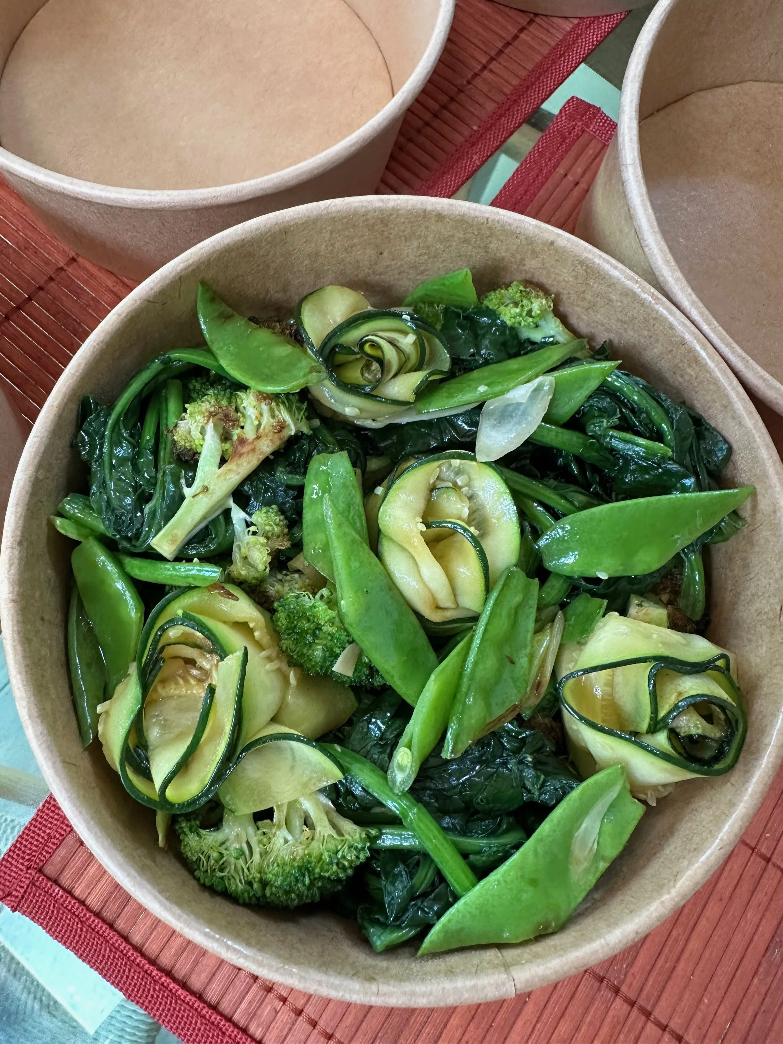 A bowl of salad made with sliced zucchini, broccoli, spinach, and snap peas.