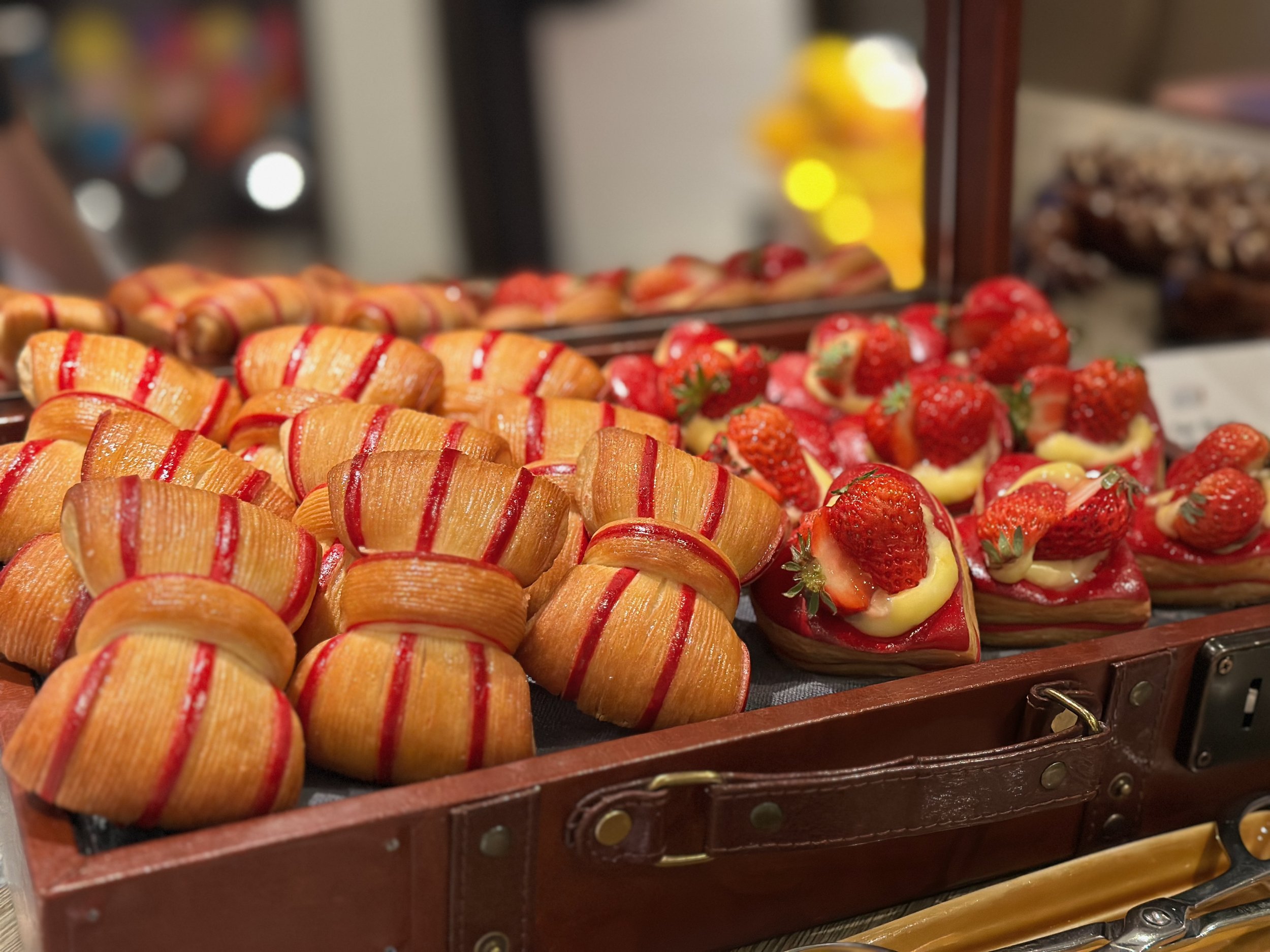 Freshly baked strawberry desserts and pastries displayed in a wooden tray at a bakery.