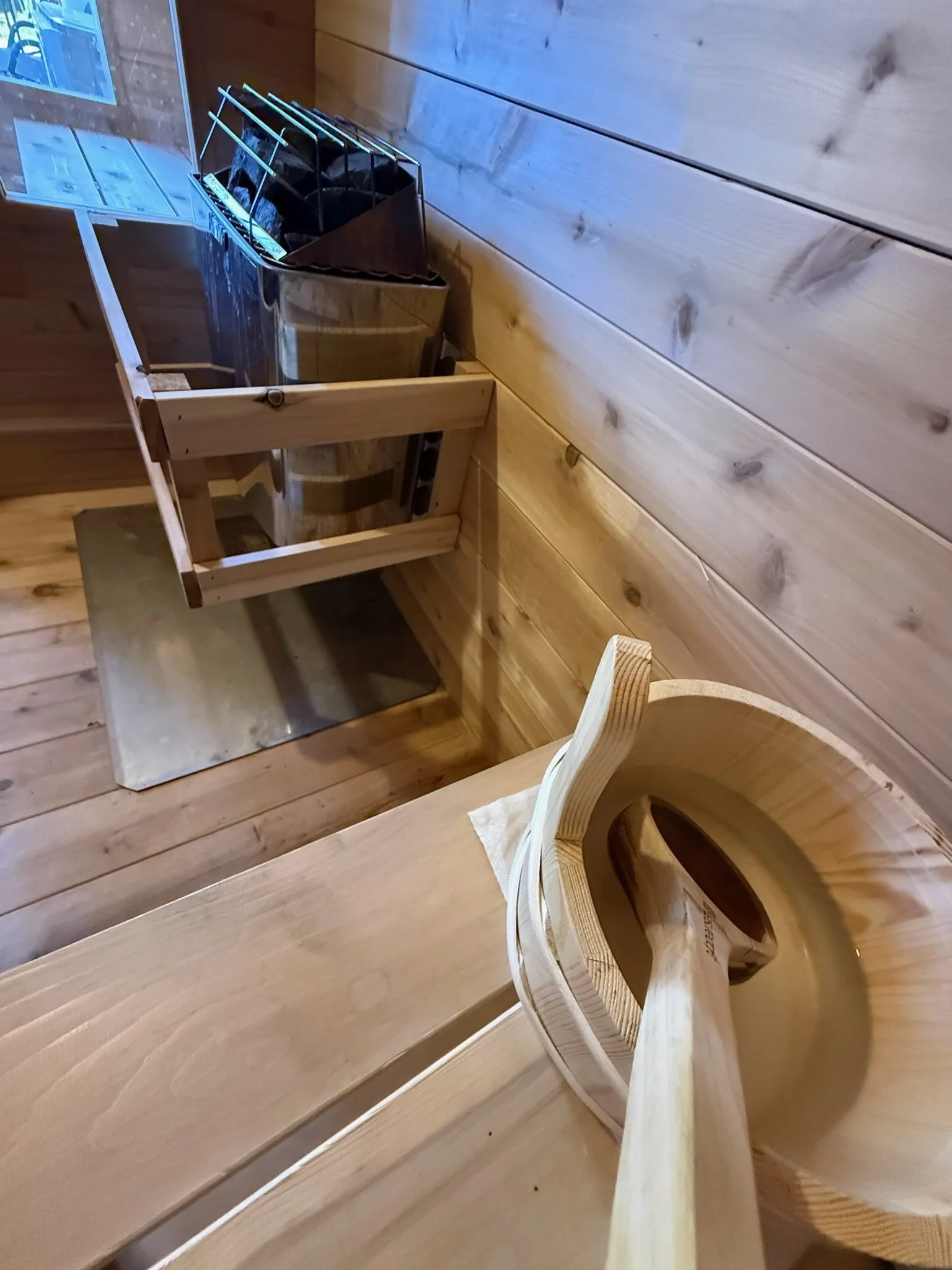 Interior of a wooden sauna room with a corner bucket, a small wooden bench, and a wooden stool.