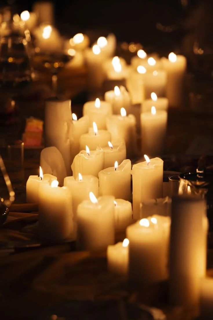 Multiple white candles burning in a dark setting, creating a warm, glowing ambiance.