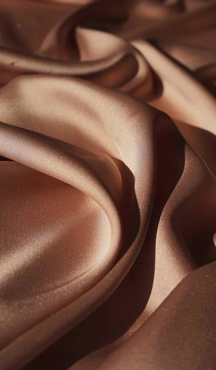 Close-up of silky, champagne-colored satin fabric with flowing, folded texture.