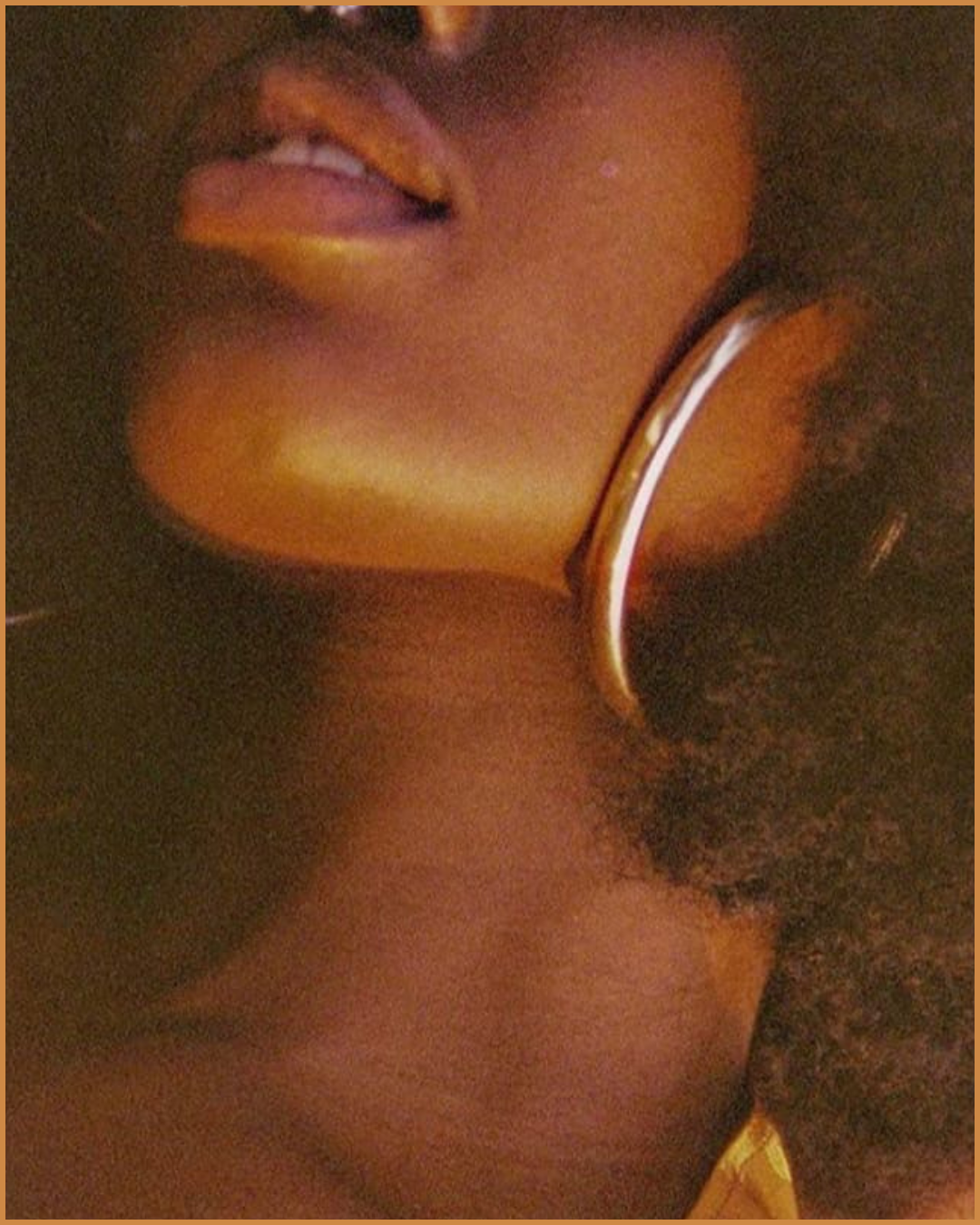Close-up of a person wearing a silver hoop earring, with their lips slightly parted and tongue sticking out, showing part of their face and neck.