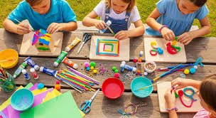 Children crafting and painting with various arts and craft supplies on a wooden table.