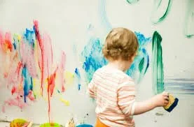 Child drawing on a wall with colorful paint