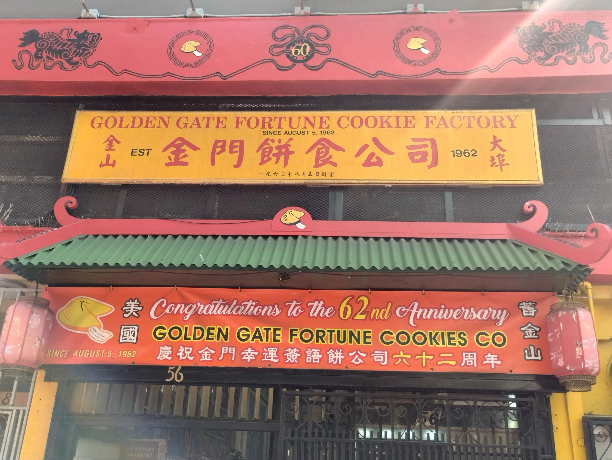 Sign for Golden Gate Fortune Cookies Co. with dragon and lion images, celebrating the company's 62nd anniversary, established August 5, 1962, in Chinese and English.