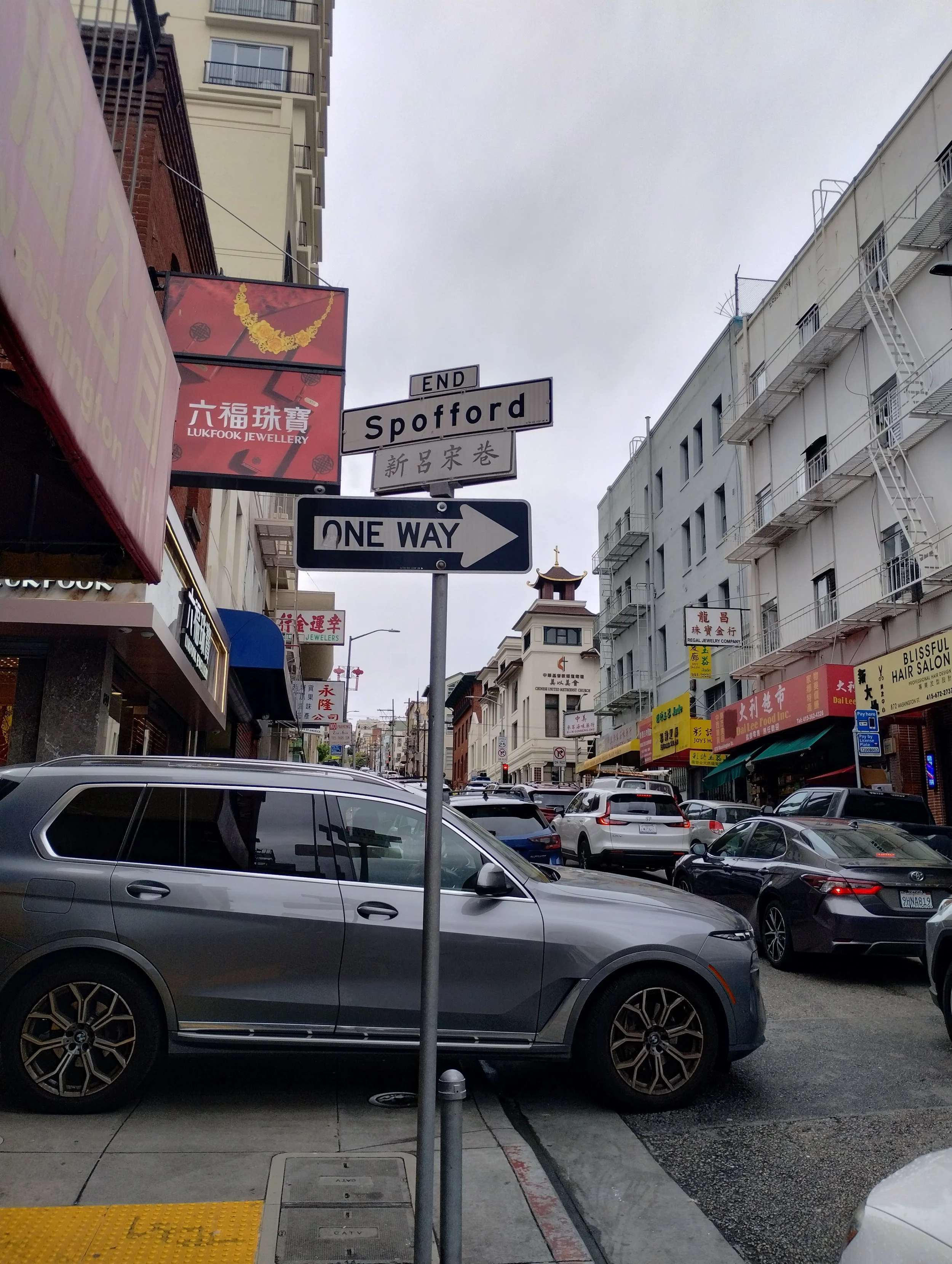 Street scene on Spofford Street with parked cars, storefronts with signs, and a cloudy sky overhead.