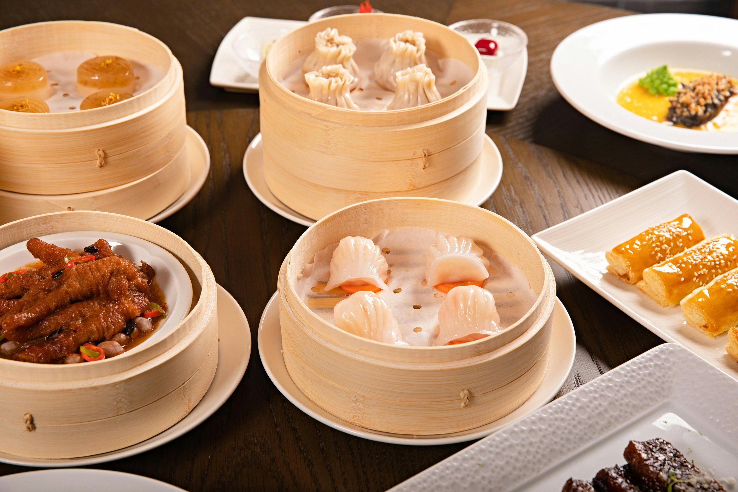 Assorted Asian dim sum dishes, including steamed dumplings in bamboo steamers, served on a wooden table.