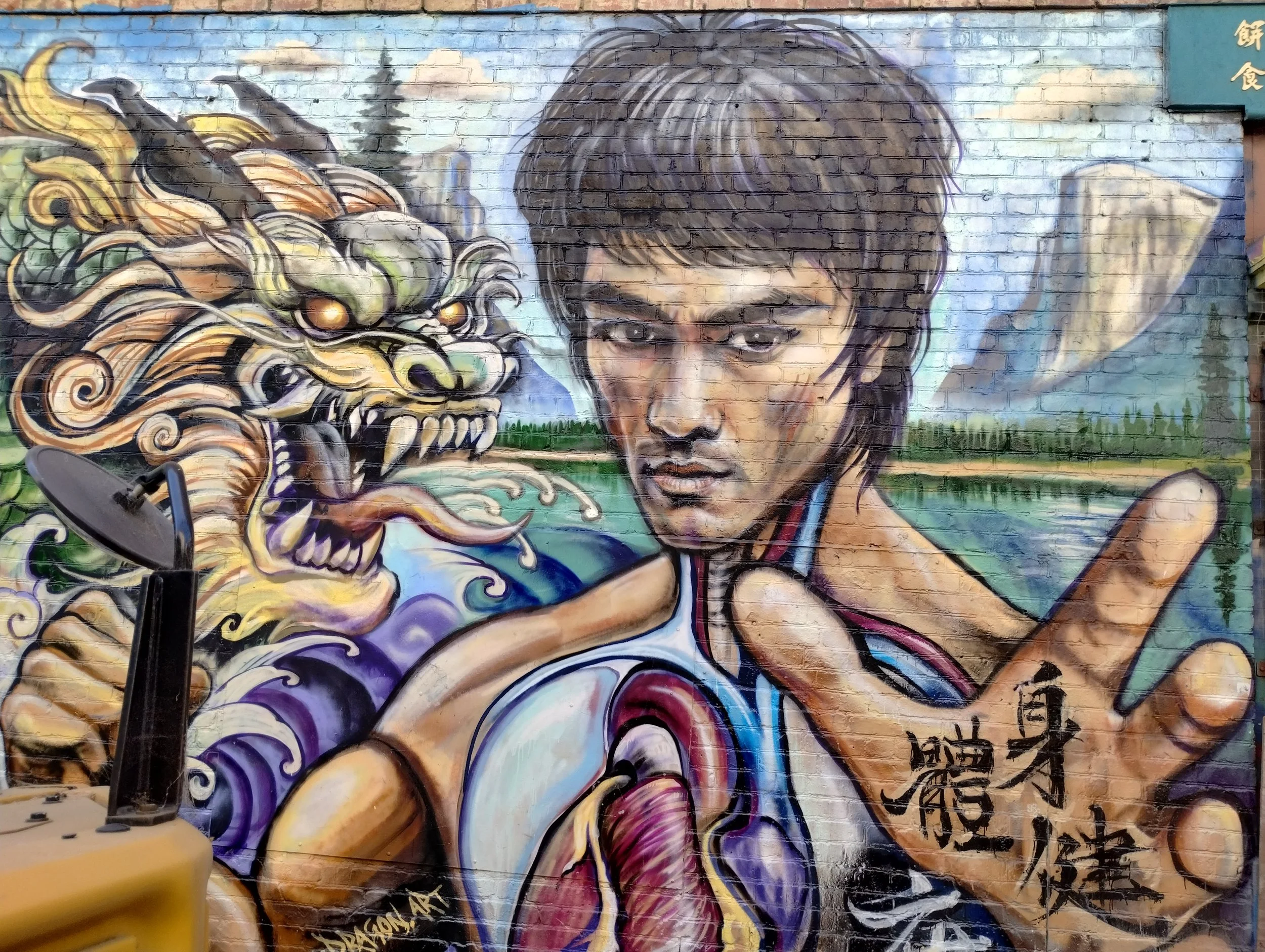 Colorful mural on a brick wall depicting a woman with dark hair and a fierce expression, accompanied by a stylized dragon with orange and yellow scales and sharp teeth, with Chinese characters and a landscape with trees and clouds in the background.