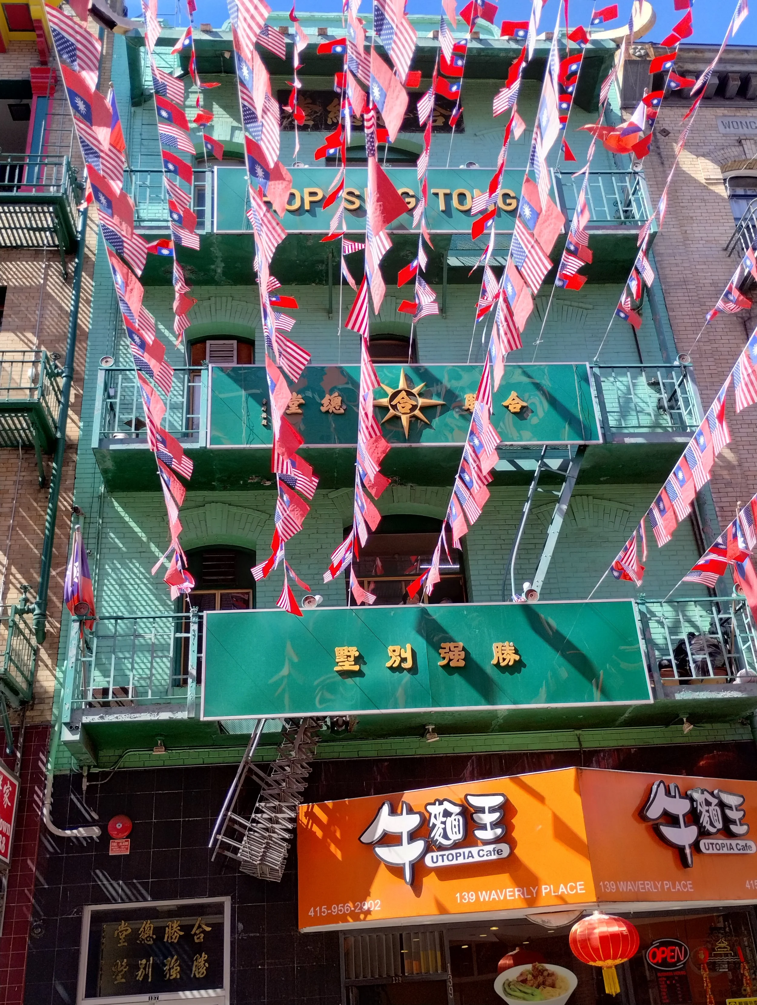 Multiple American and Taiwanese flags hanging in front of a building, with signs for a cafe named UTOPIA Cafe and Chinese characters on the building and a sign in the window.