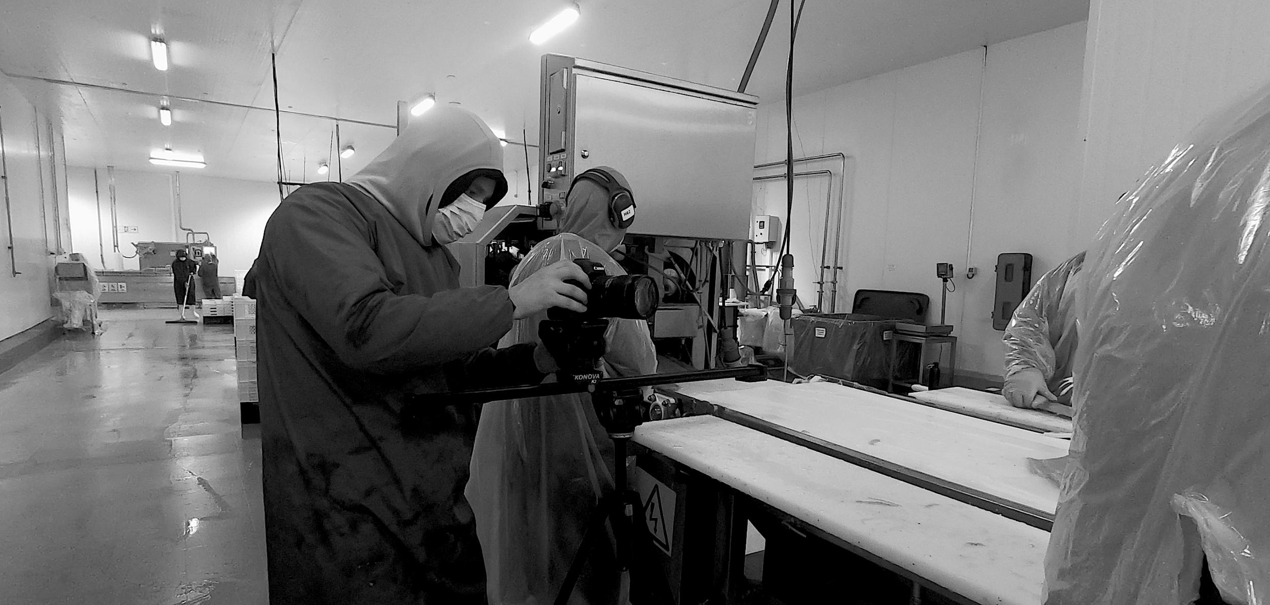 Personal en un ambiente industrial, con uno enfocando una máquina y otro con equipo de protección en un espacio de trabajo