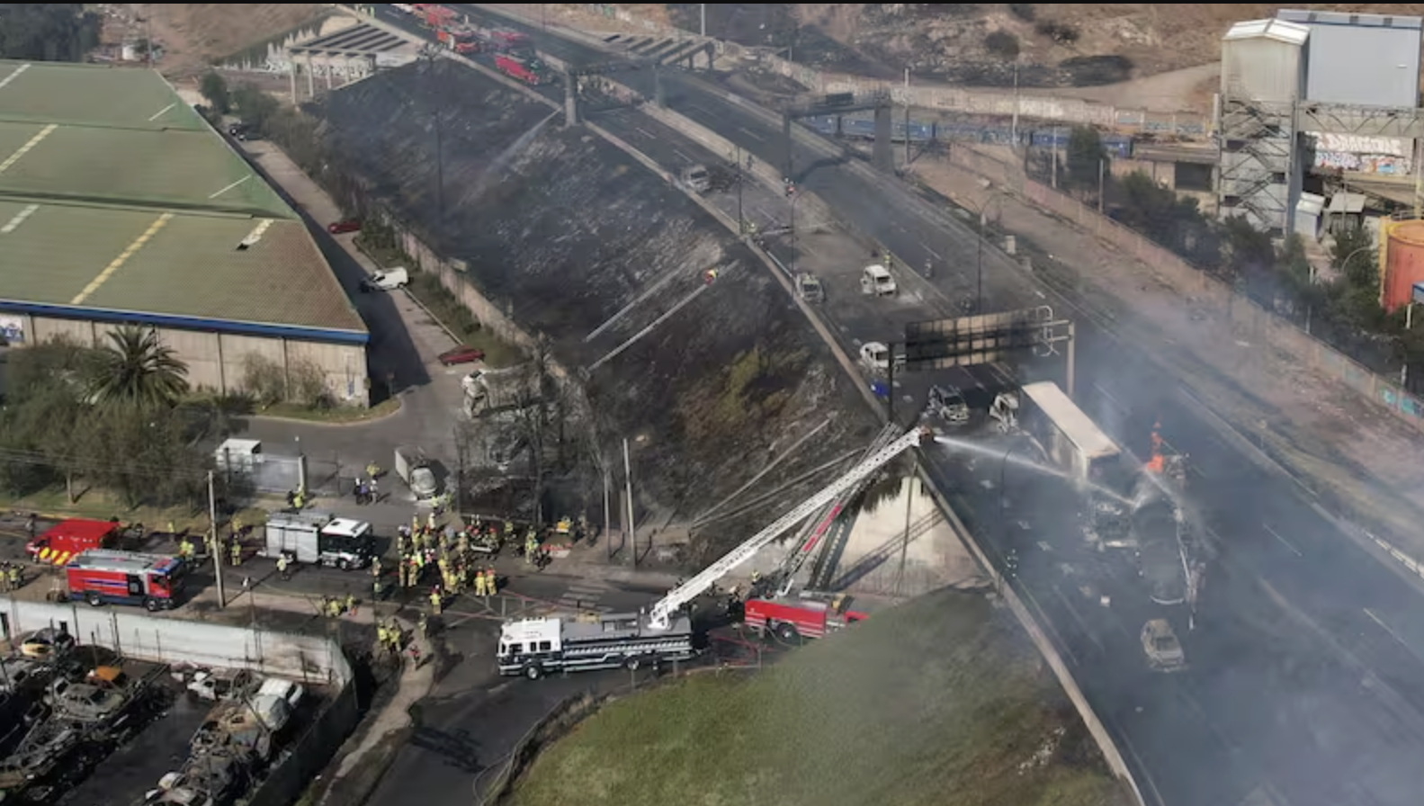 Incendio y accidente en una autopista con bomberos y personal de emergencia trabajando en la escena.