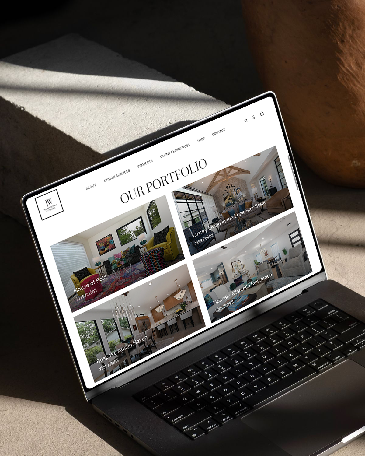 A laptop screen displaying a portfolio website with images of interior design projects, including a colorful living room, luxury living in the Lone Star State, a modern kitchen, and a stylish residence for John-William Interiors in Austin, Texas.