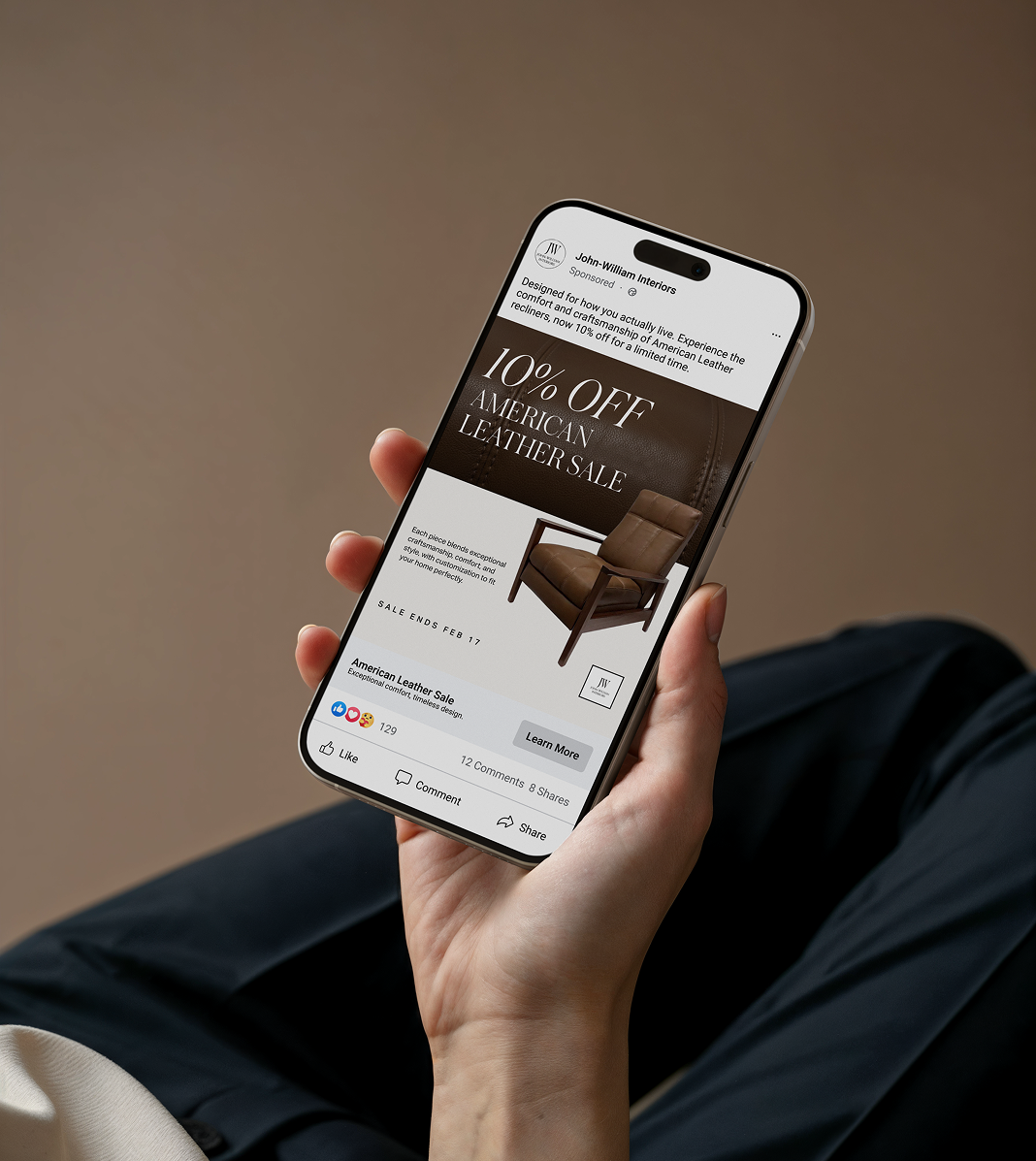 A person holding a smartphone displaying an American leather sale advertisement with furniture images and discount details.