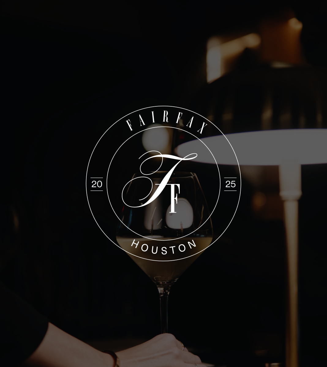 Glass of white wine on a table with a dark background and a lamp in the background, featuring a logo for Fairfax Houston.