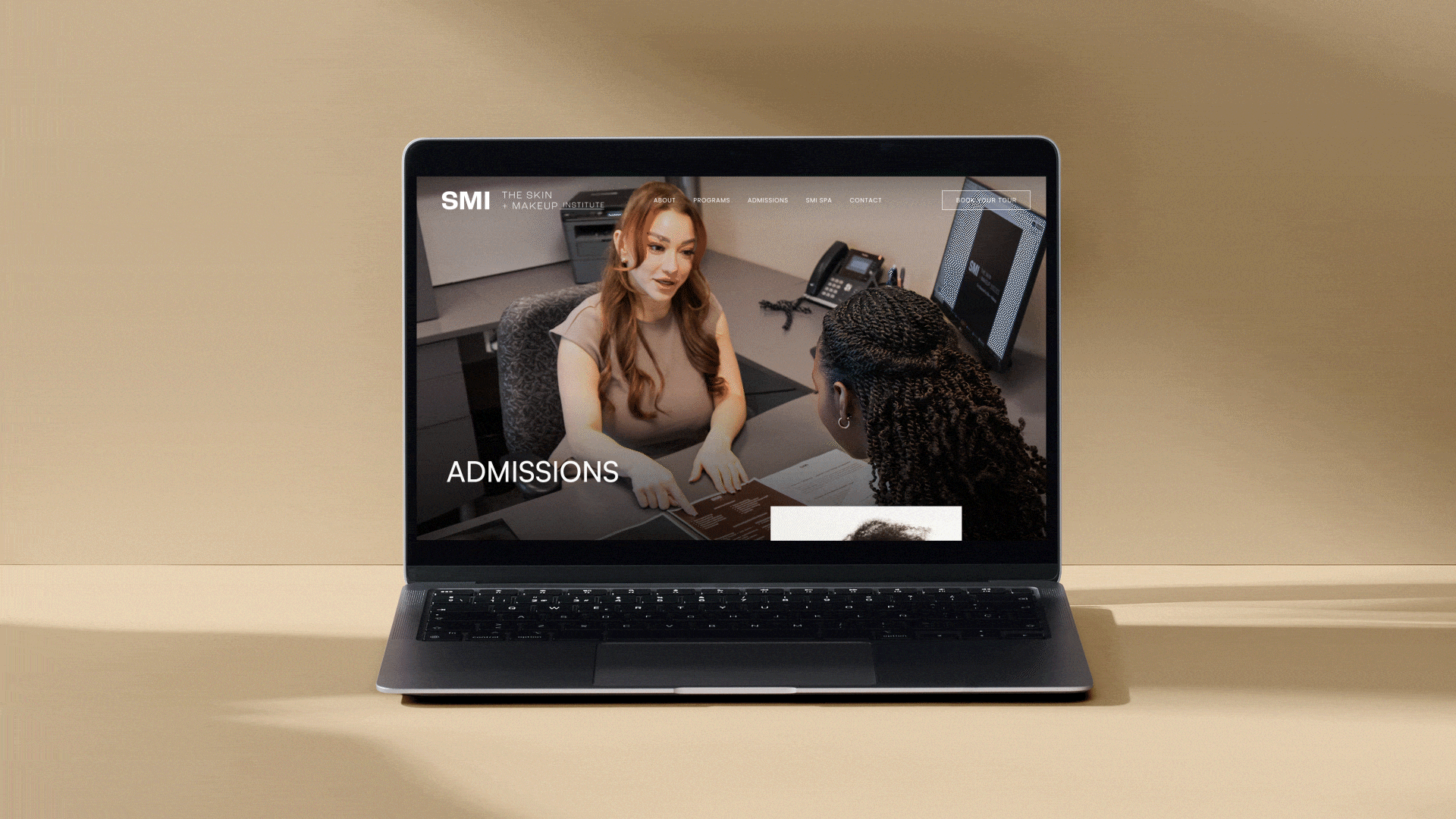 Laptop displaying a webpage for The Skin + Makeup Institute, showing a woman interviewing a client at a desk inside an office.