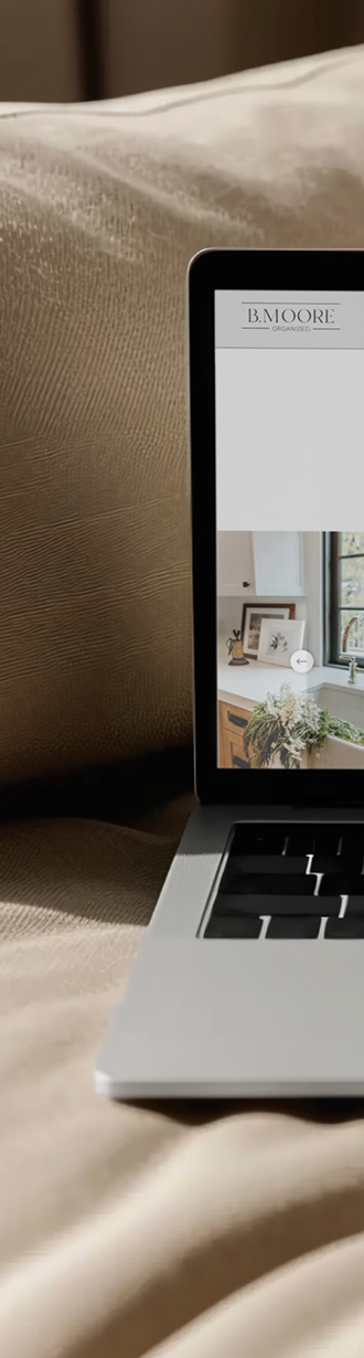 Laptop on a bed displaying a room with framed artwork and a window with natural light.