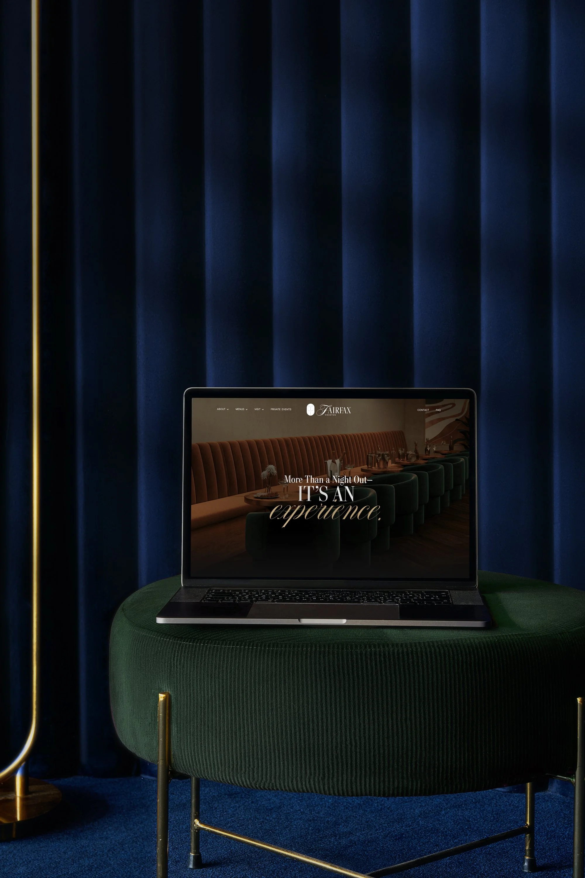 Laptop on a green velvet chair with a navy blue curtain background, displaying a website with an interior dining scene and text reading 'More Than a Night Out, IT'S AN experience" for Fairfax Cocktail Bar in Houston, Texas.