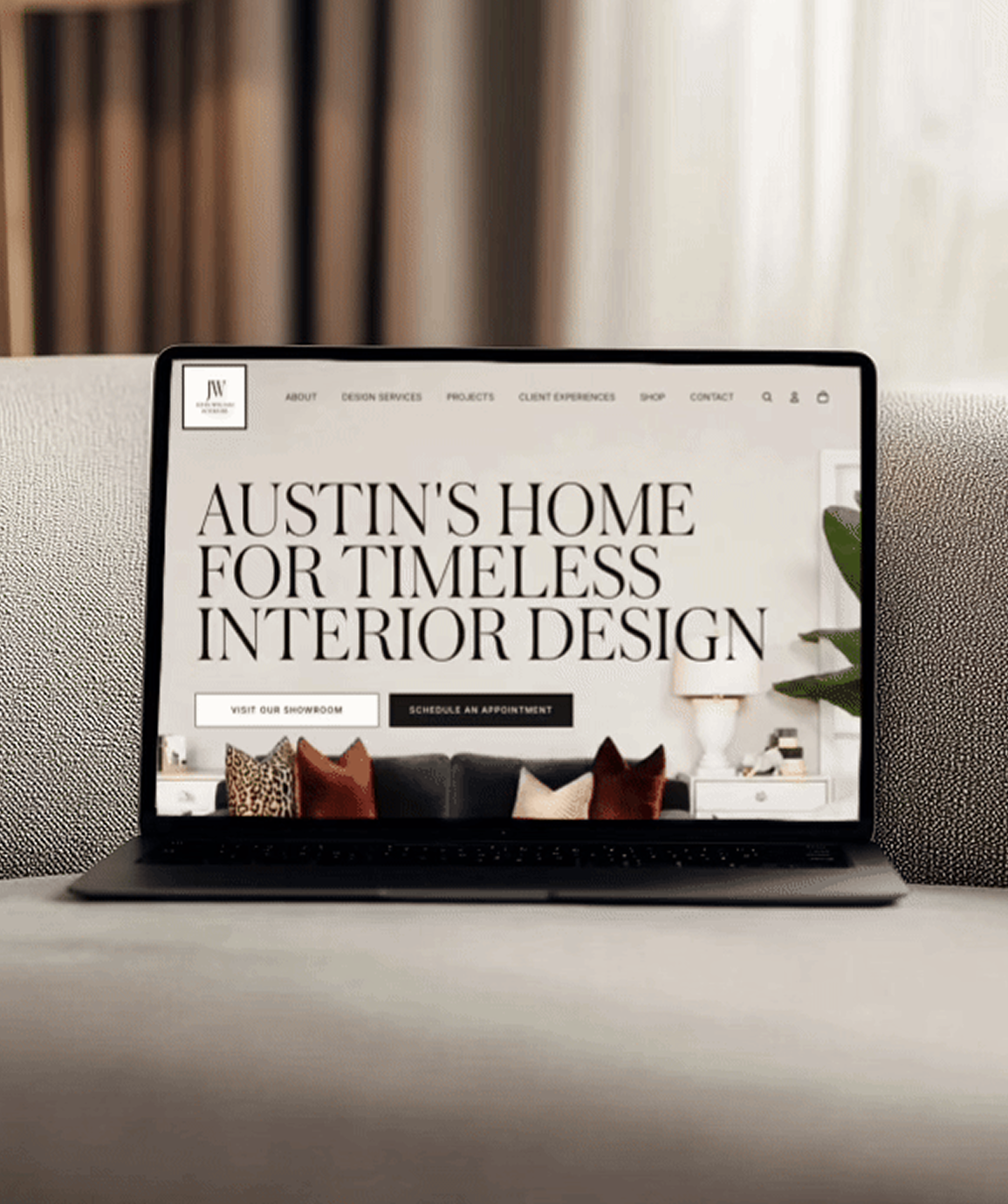 Laptop on a table displaying a website for interior design with the text "Austin's Home for Timeless Interior Design" for John-William Interiors in Austin, Texas.