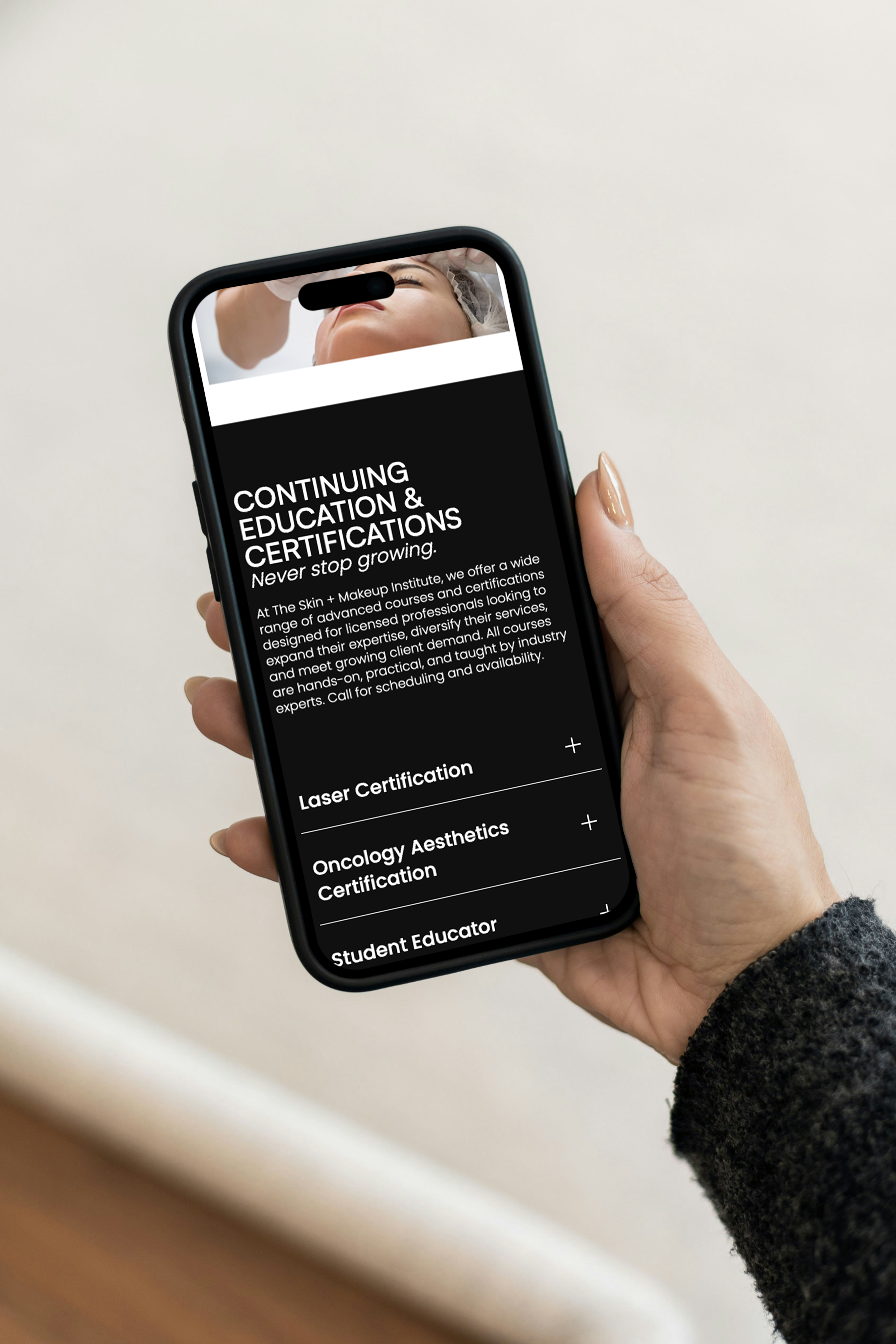 Person holding a smartphone displaying a website about continuing education and certifications for a skincare institute, including laser certification, oncology aesthetics, and student educator programs.