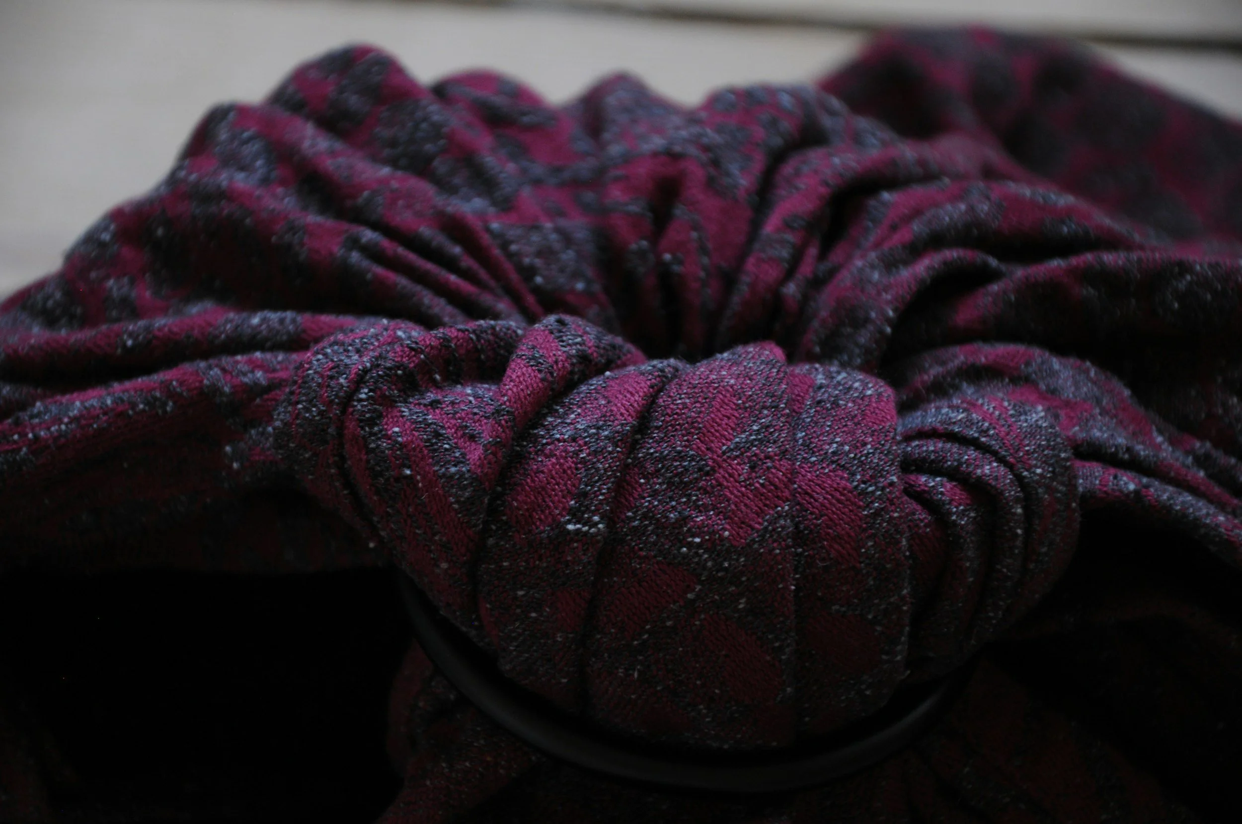 A close-up of a scrunchie made from a red and black plaid fabric with a textured pattern, resting on a black surface.
