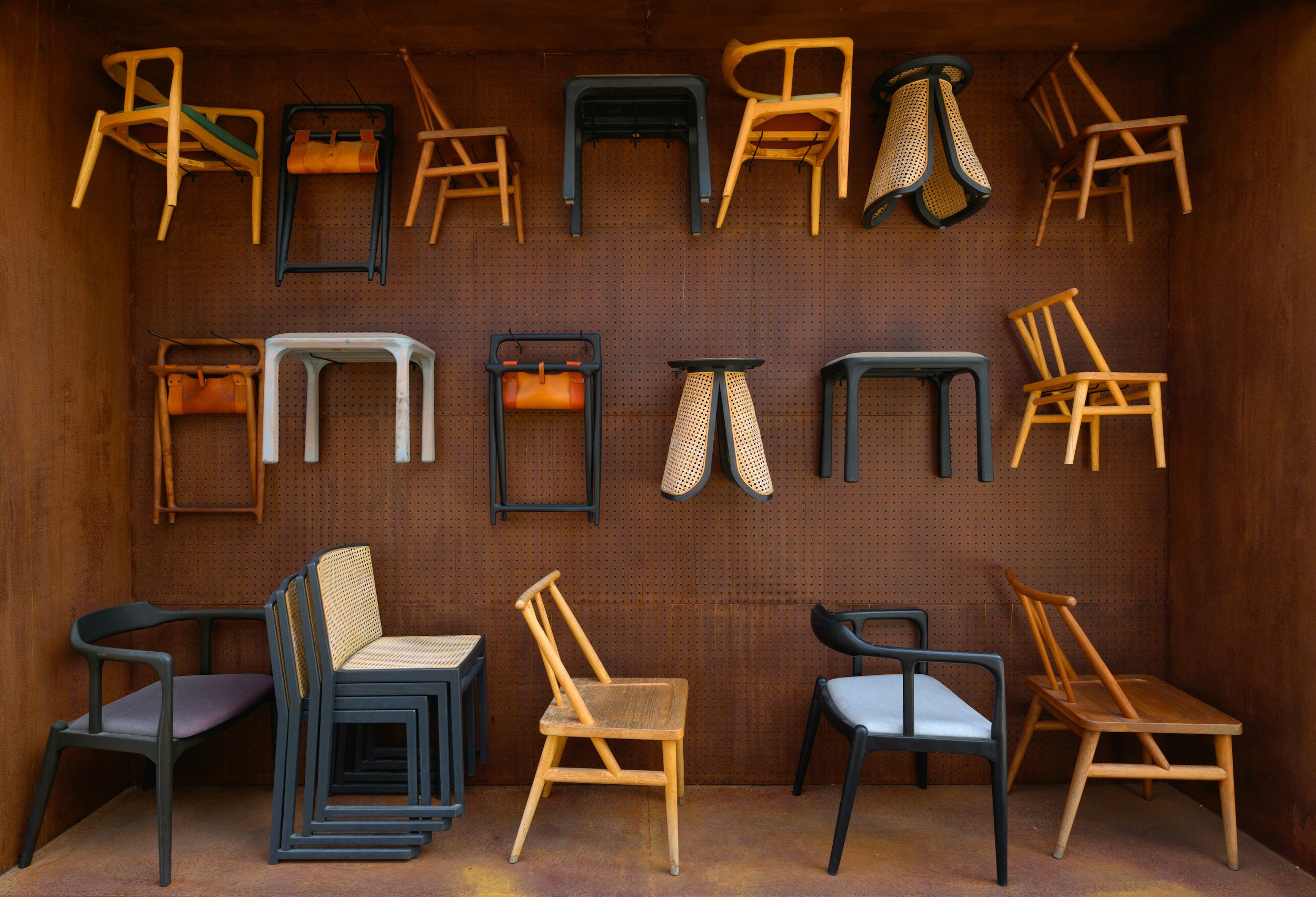 Various chairs and stools mounted on a wooden pegboard wall inside a wooden room.
