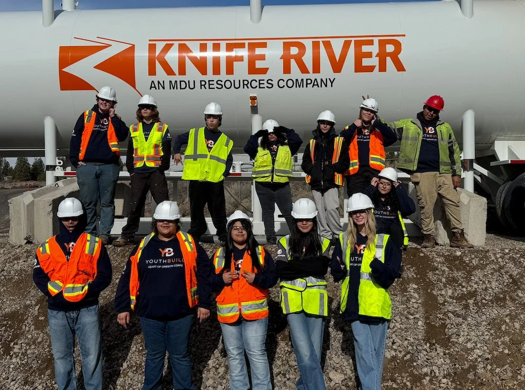 Group of young people in safety vests and hard hats standing in front of a large industrial tank with the logo 'Knife River' and text 'An MDU Resources Company'.