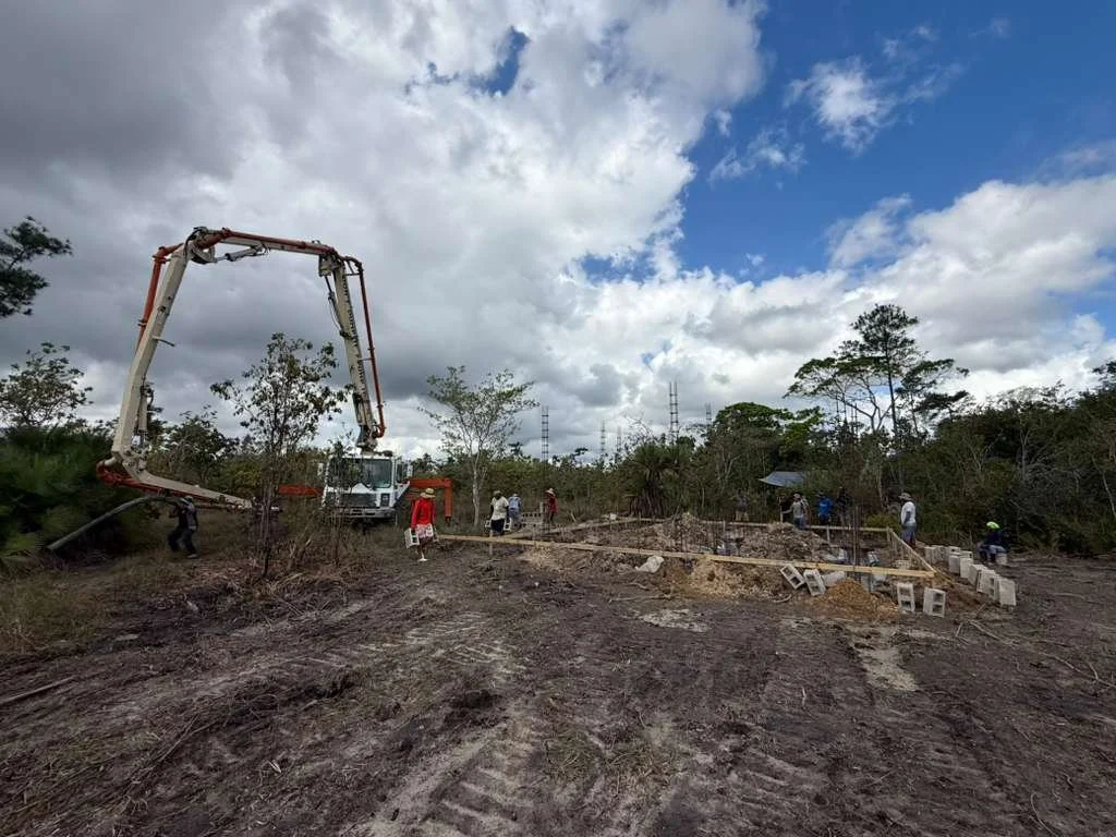 Construction site with workers, a concrete pump truck, and foundation work in progress under cloudy sky.