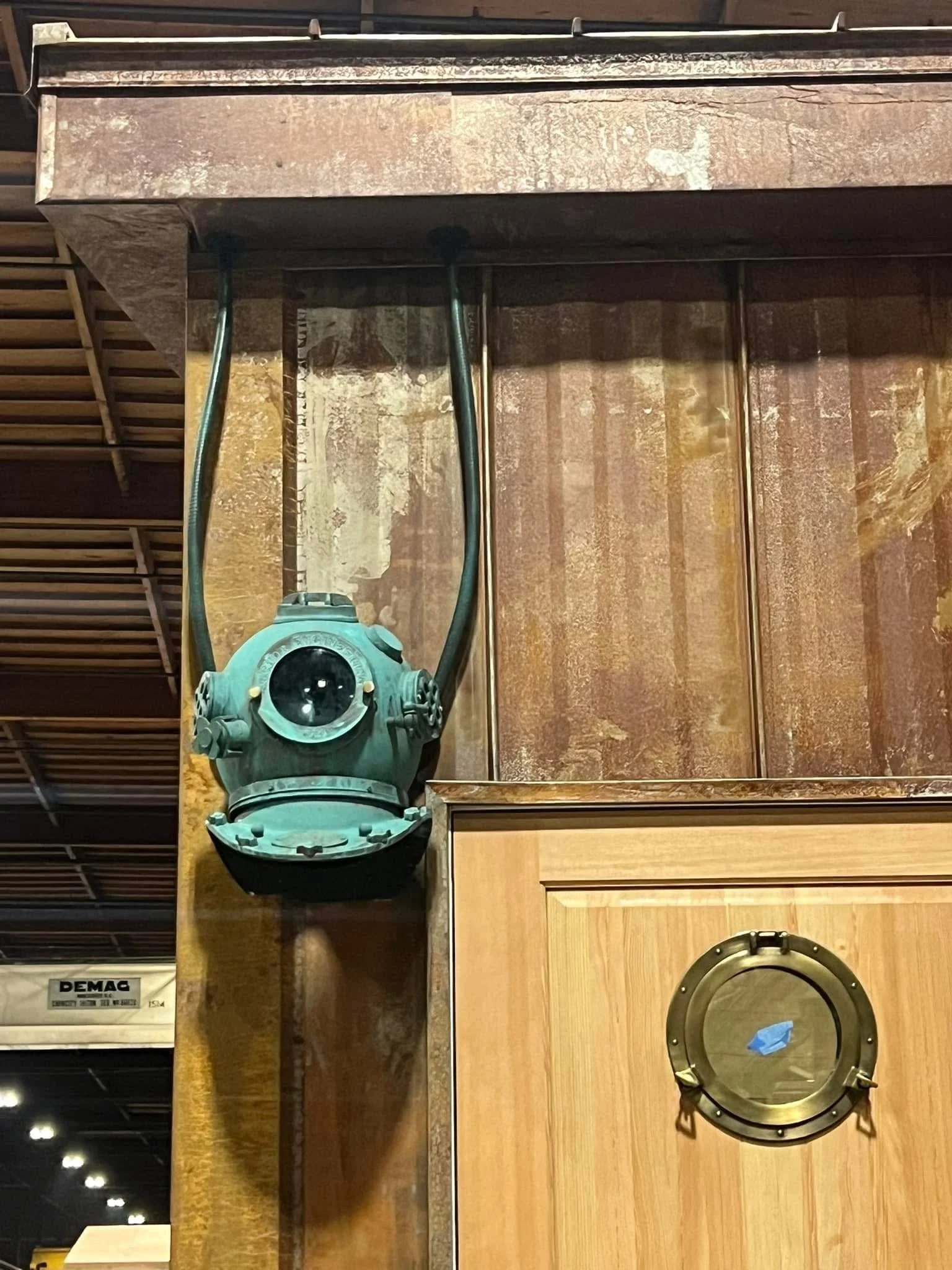 Two speakers and a laser level on a wooden surface with various wood and metal panels, with ceiling lights visible in the background.