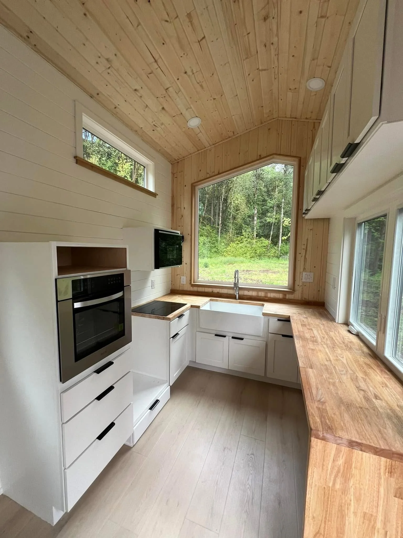 A kitchen with a wooden ceiling and large window overlooking a forest.