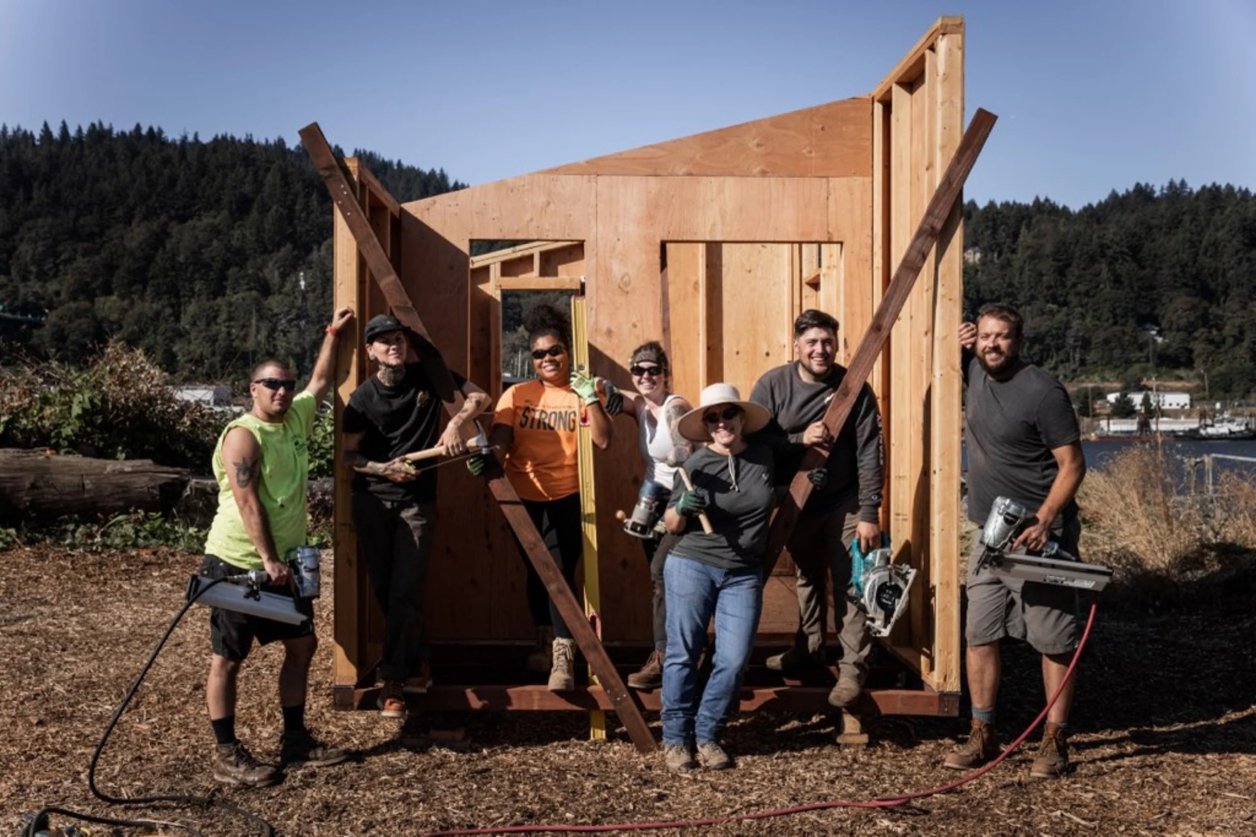 A group of people working together on a wooden construction project outdoors with mountains in the background.