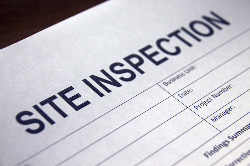 Close-up photo of a site inspection report form on a wooden desk, showing the title and blank fields for business details and findings.