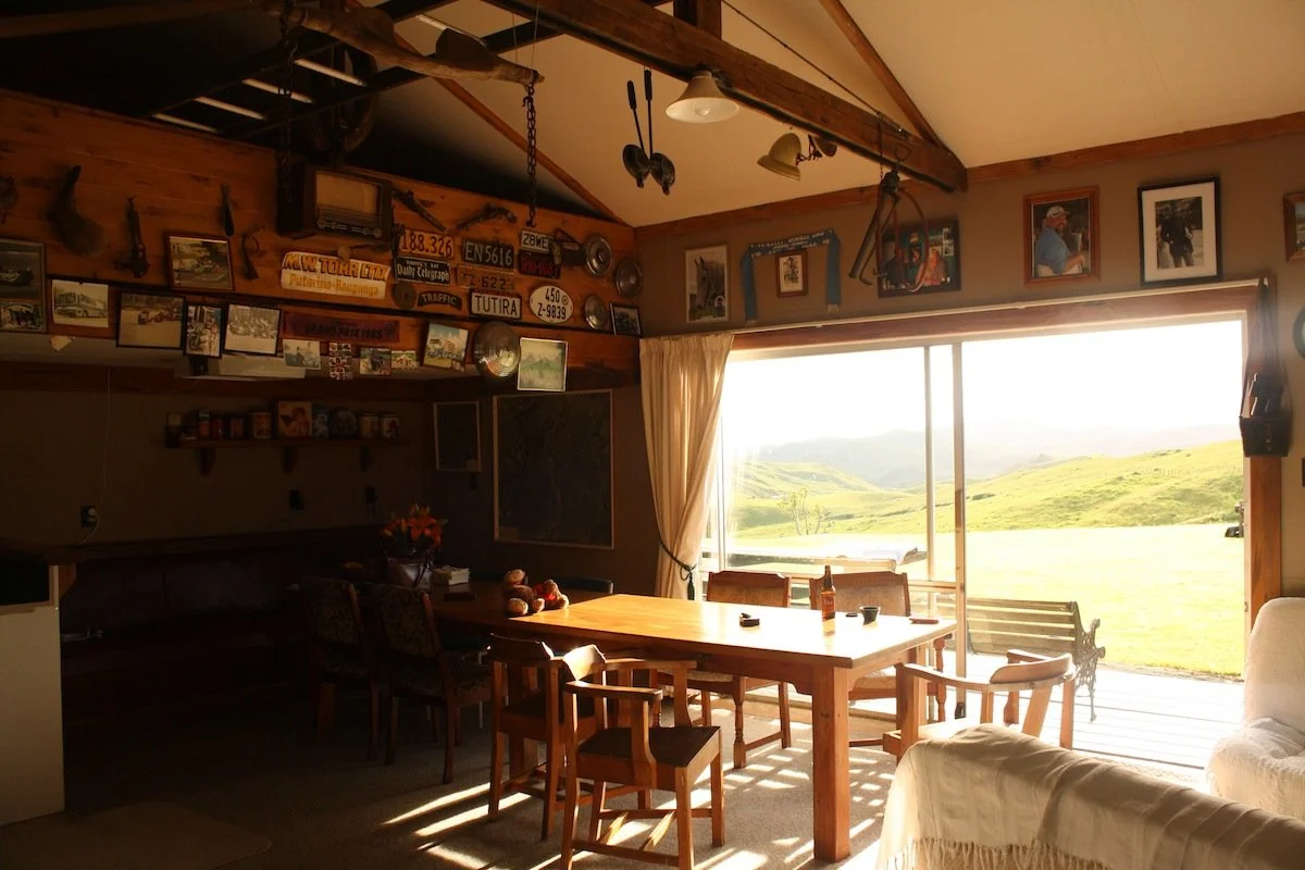 Cozy dining area with wooden furniture and large window overlooking green rolling hills and a bright outdoor scene.