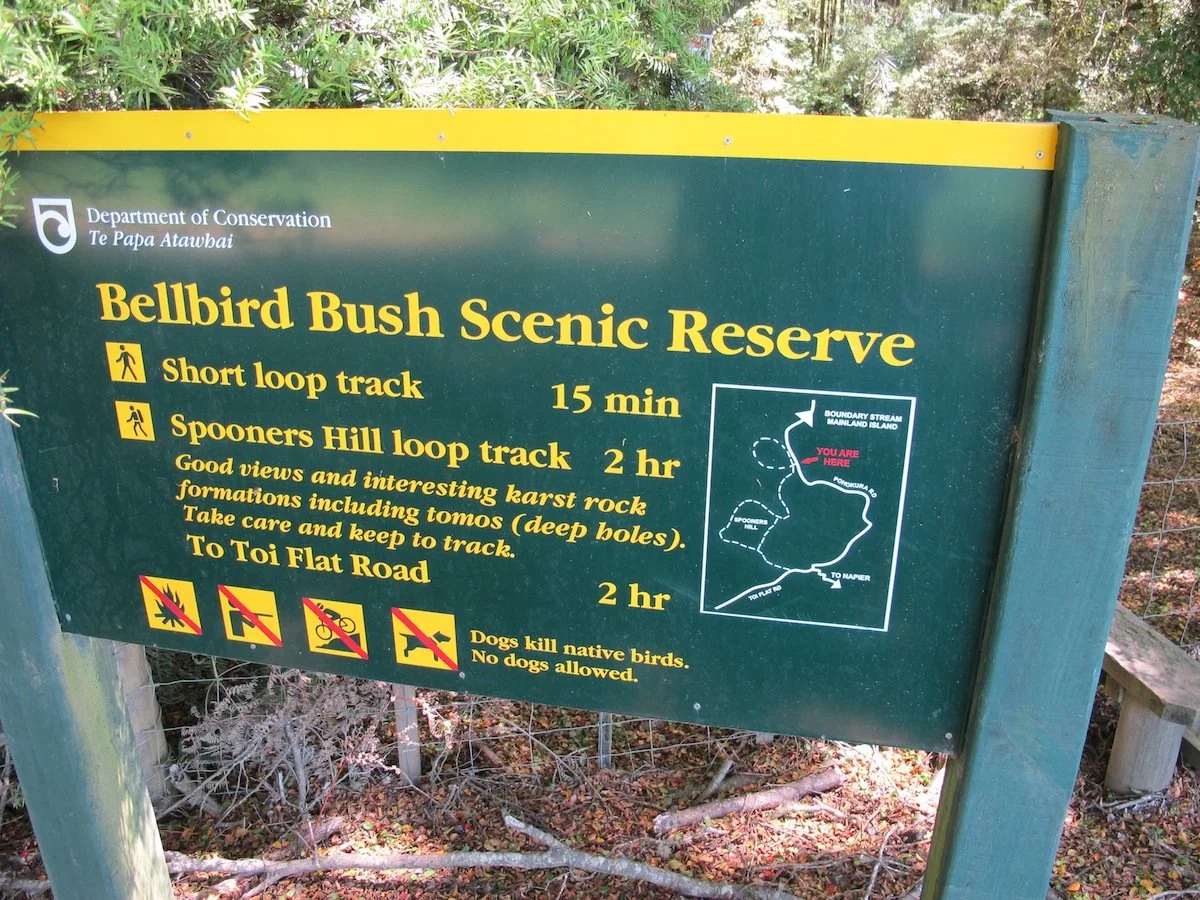 Sign for Bellbird Bush Scenic Reserve with trail information, map, and symbols indicating no fires, no dogs, and no bicycles.