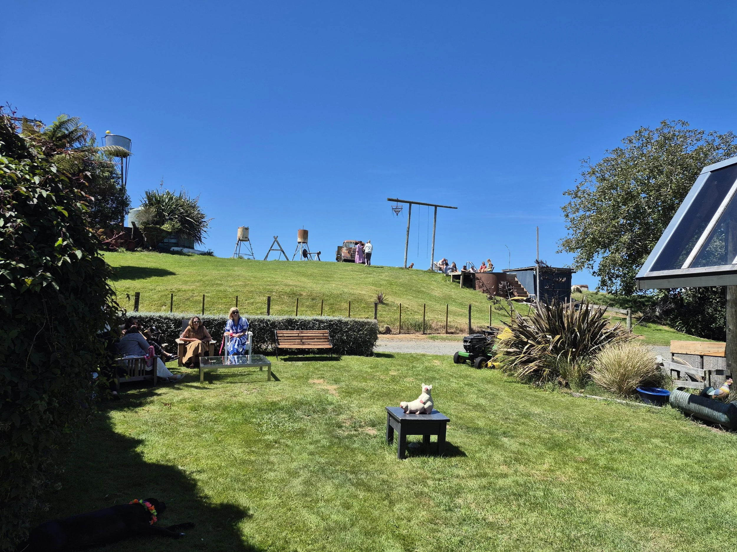 Lawn with small animal figurines, benches, and people sitting and standing on a hill under a clear blue sky.