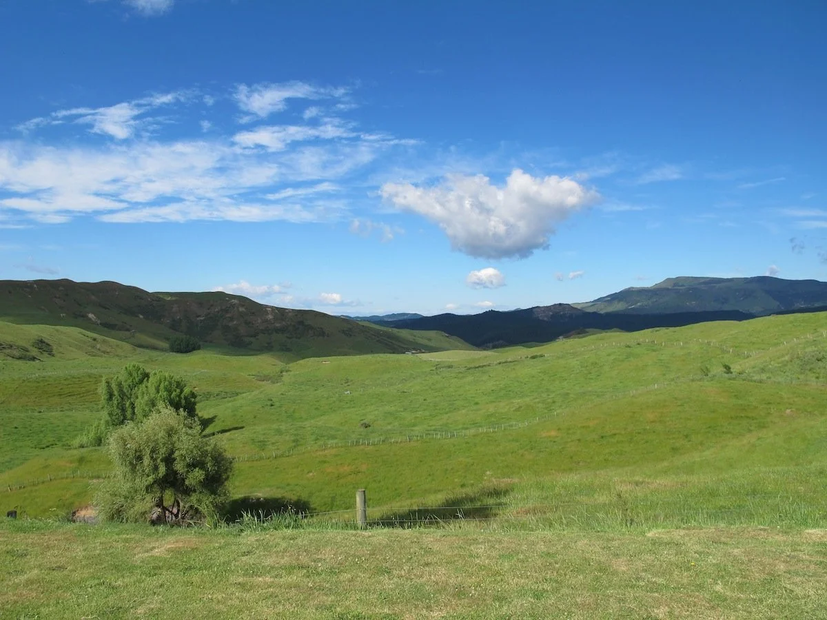 Green rolling hills under a blue sky with scattered clouds.