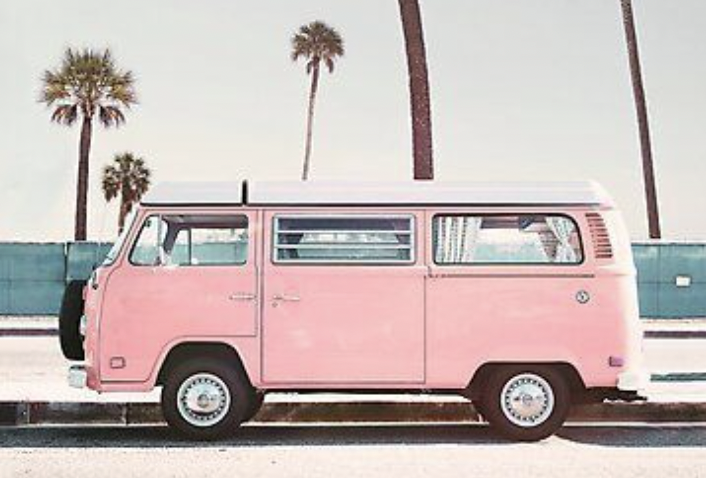 A pink vintage van parked on the side of a street with palm trees in the background.