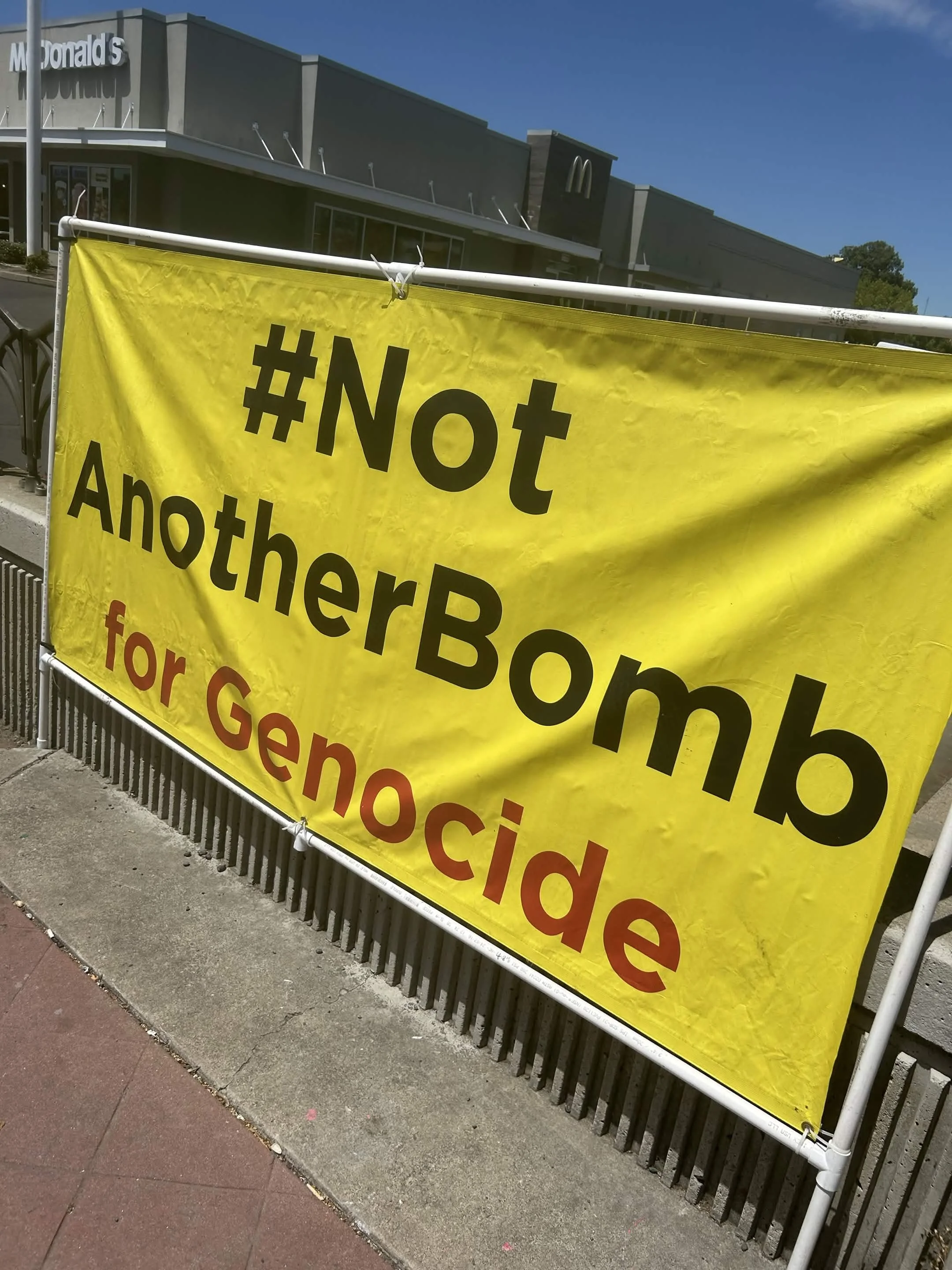 A large yellow banner with black and red text #notanotherbombforgenocide